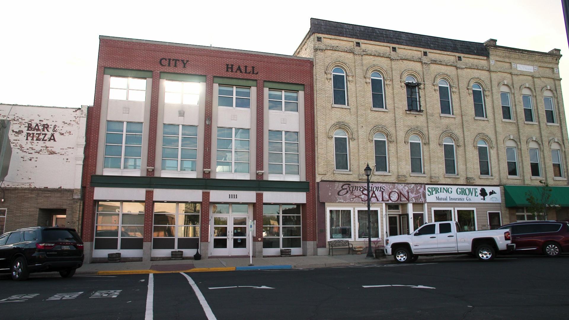 A view of the front of Brodhead's brick city hall, with cars parked in the foreground.