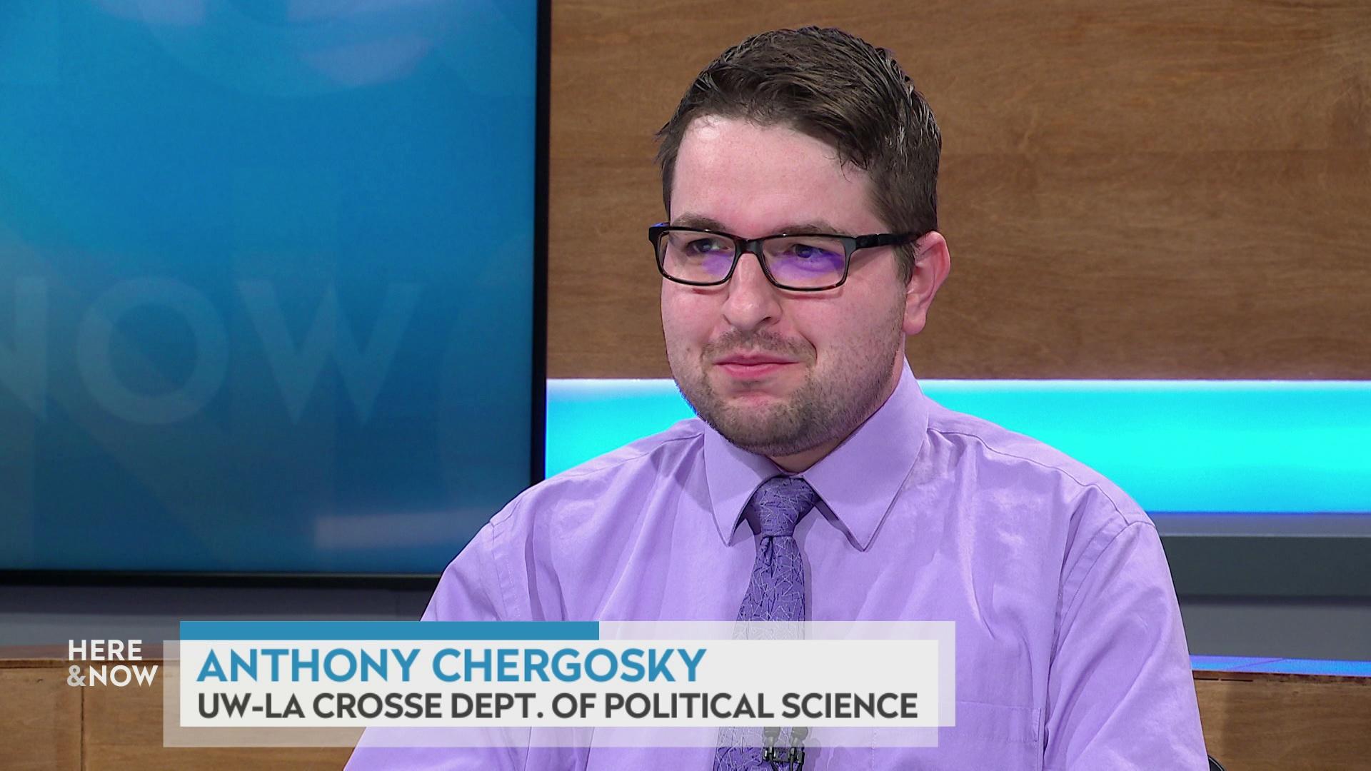 A still image shows Anthony Chergosky seated at the 'Here & Now' set featuring wood paneling, with a graphic at bottom reading 'Anthony Chergosky' and 'UW-La Crosse Dept. of Political Science.'