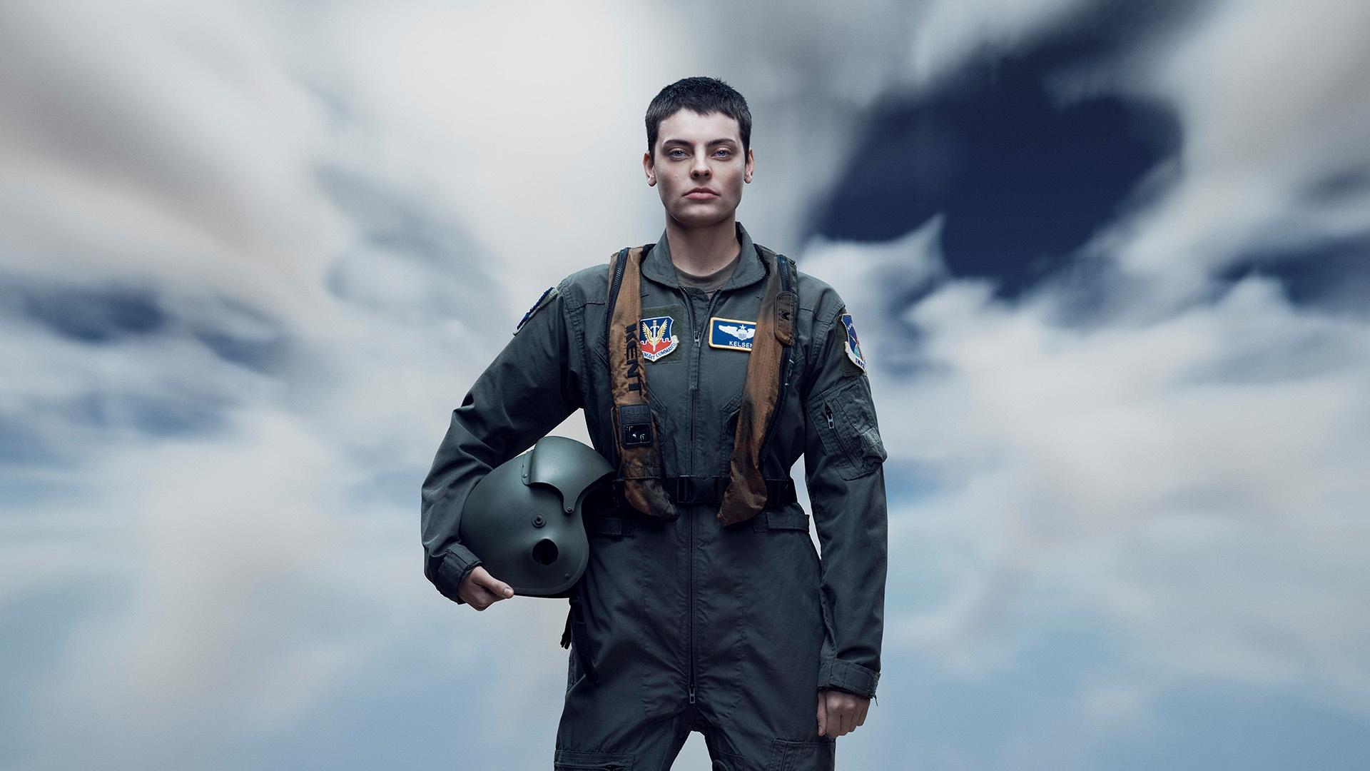 Fighter pilot stands against sky with clouds.