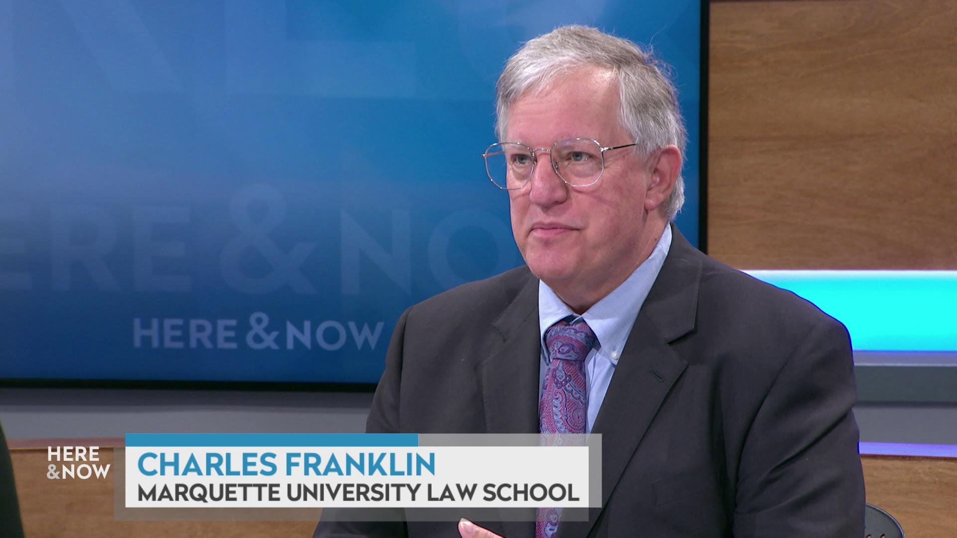 A still image shows Charles Franklin seated at the 'Here & Now' set featuring wood paneling, with a graphic at bottom reading 'Charles Franklin' and 'Marquette University Law School.'