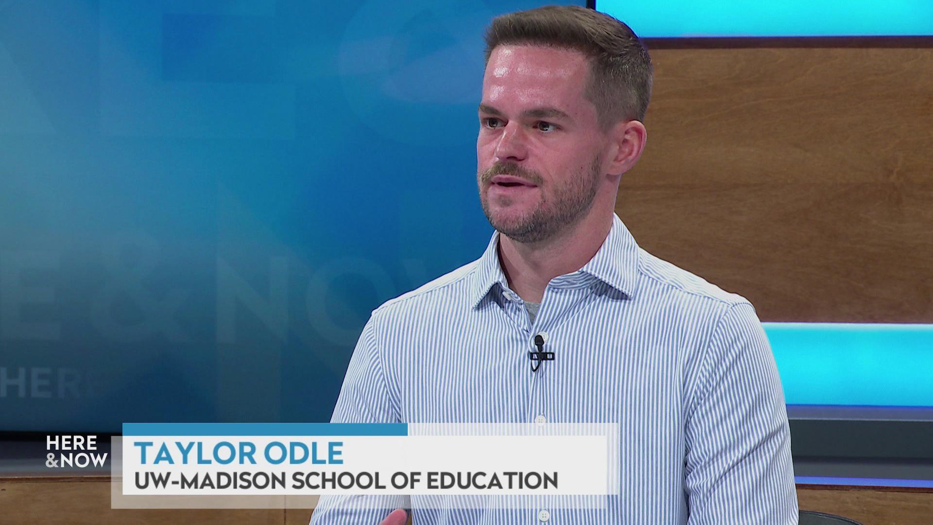 A still image shows Taylor Odle seated at the 'Here & Now' set featuring wood paneling, with a graphic at bottom reading 'Taylor Odle' and 'UW-Madison School of Education'