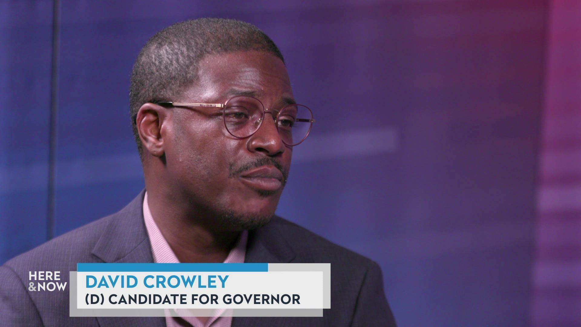 A still image shows David Crowley seated on the 'Here & Now' satellite set featuring a gradient background, with a graphic at the bottom that reads 'David Crowley' and '(D) Candidate for Governor.' A still image shows David Crowley seated on the 'Here & Now' satellite set featuring a gradient background, with a graphic at the bottom that reads 'David Crowley' and '(D) Candidate for Governor.'