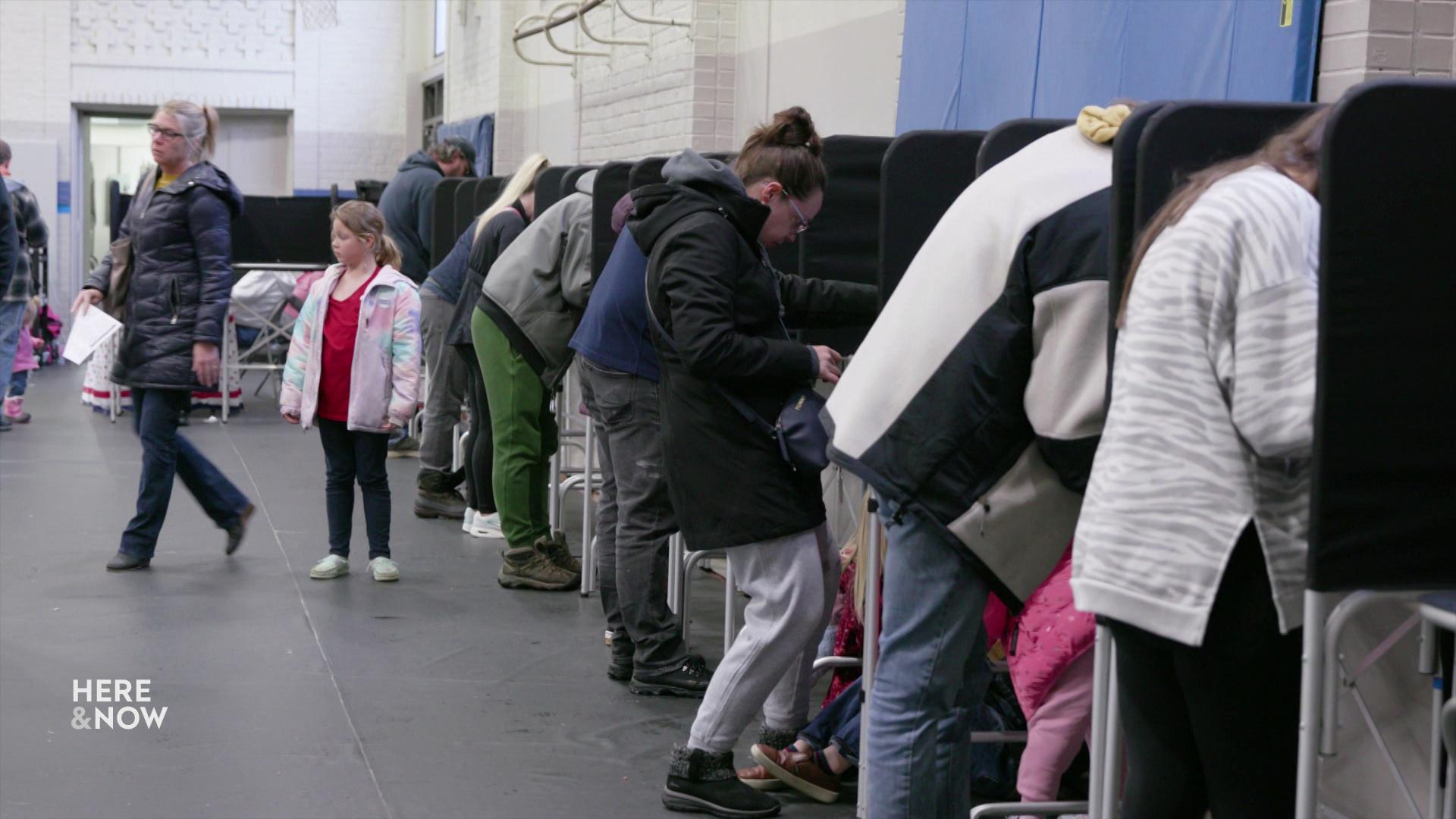 A still image shows a row of people hovered over individual booths with people walking in the background.