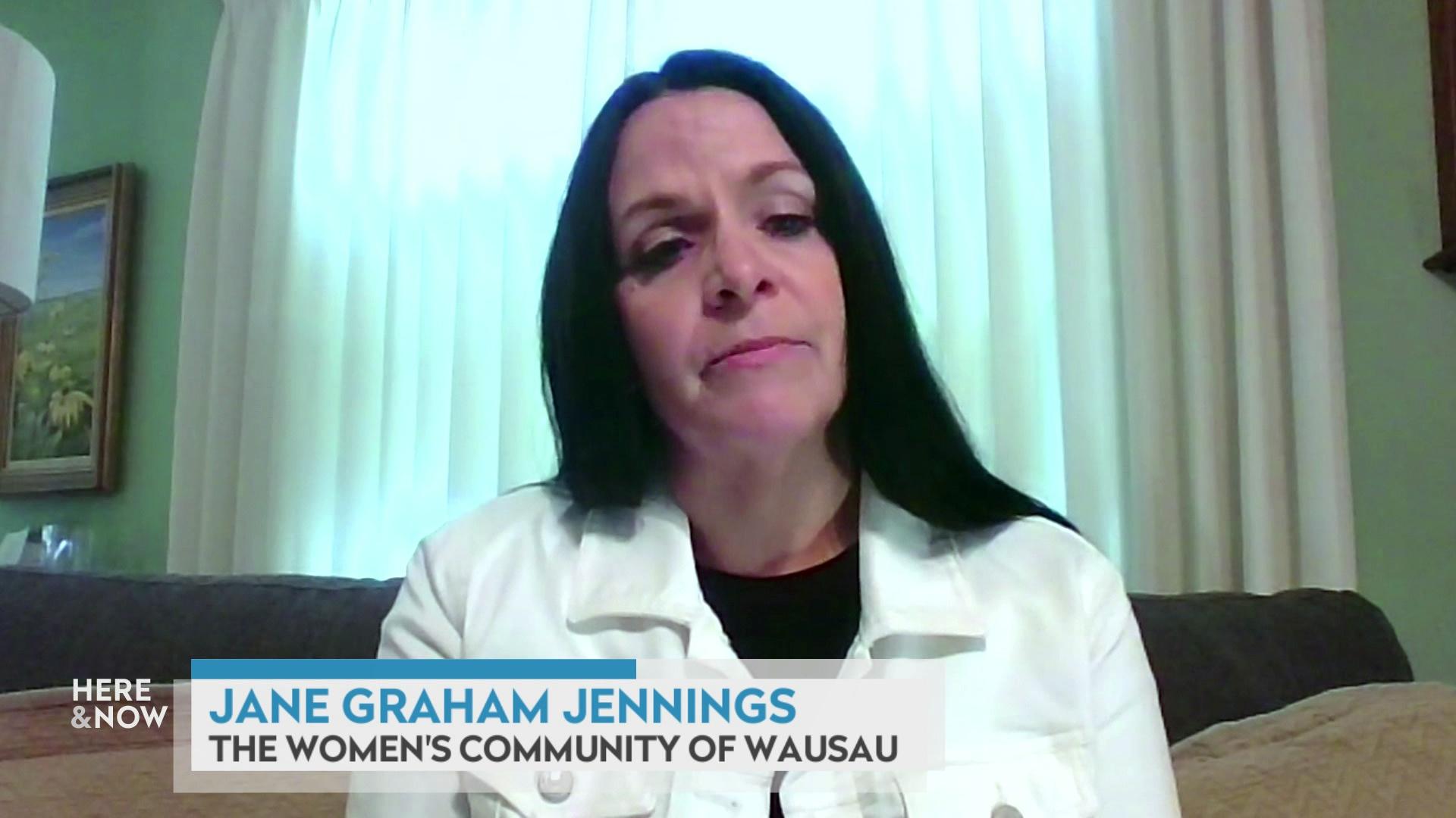 A still image from a video shows Jane Graham Jennings seated in front of a drawn white curtains and a lamp to her left with a graphic at bottom reading 'Jane Graham Jennings' and 'The Women's Community of Wausau.'