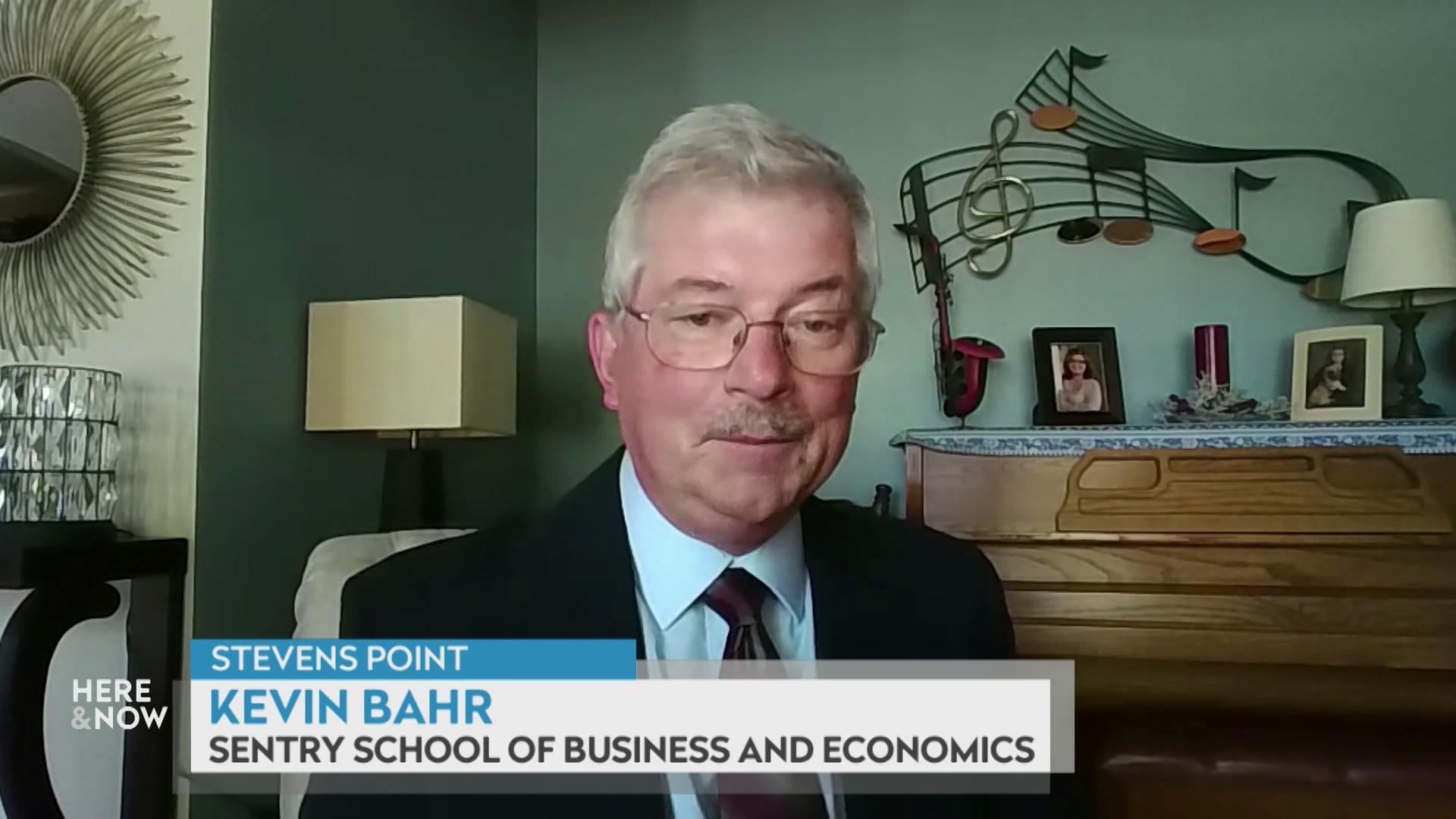 A still image from a video shows Kevin Bahr seated in front of a green wall and piano with wooden paneling with a graphic at bottom reading 'Kevin Bahr' and 'Sentry School of Business and Economics.'