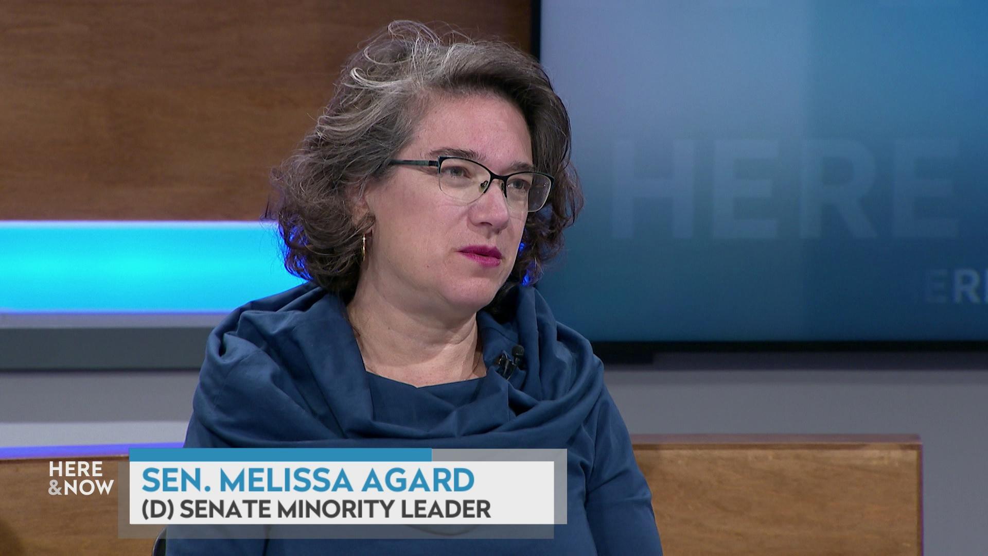 A still image shows Melissa Agard seated at the 'Here & Now' set featuring wood paneling, with a graphic at bottom reading 'Sen. Melissa Agard' and '(D) Senate Minority Leader.'