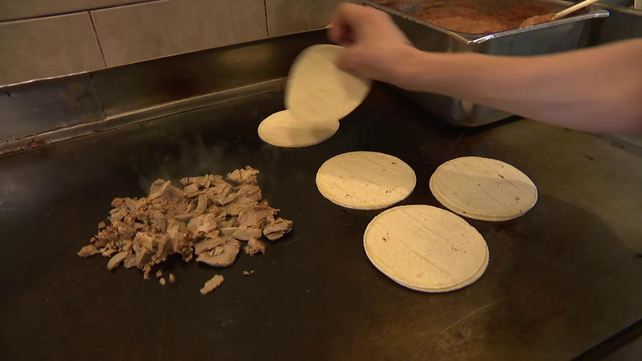 Meat and tortillas cook on a griddle as a cook ads another tortilla