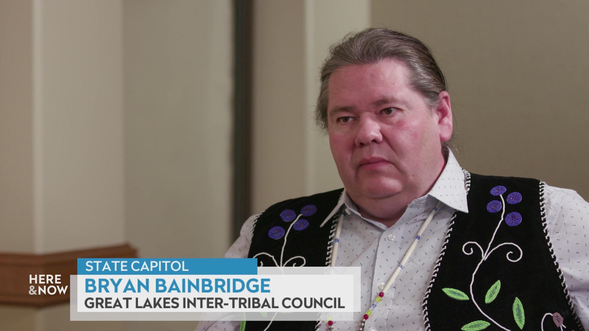A still image from a video shows Bryan BainBridge seated in front of a tan wall with a graphic at bottom reading 'State Capitol,' 'Bryan BainBridge' and 'Great Lakes Inter-Tribal Council.'
