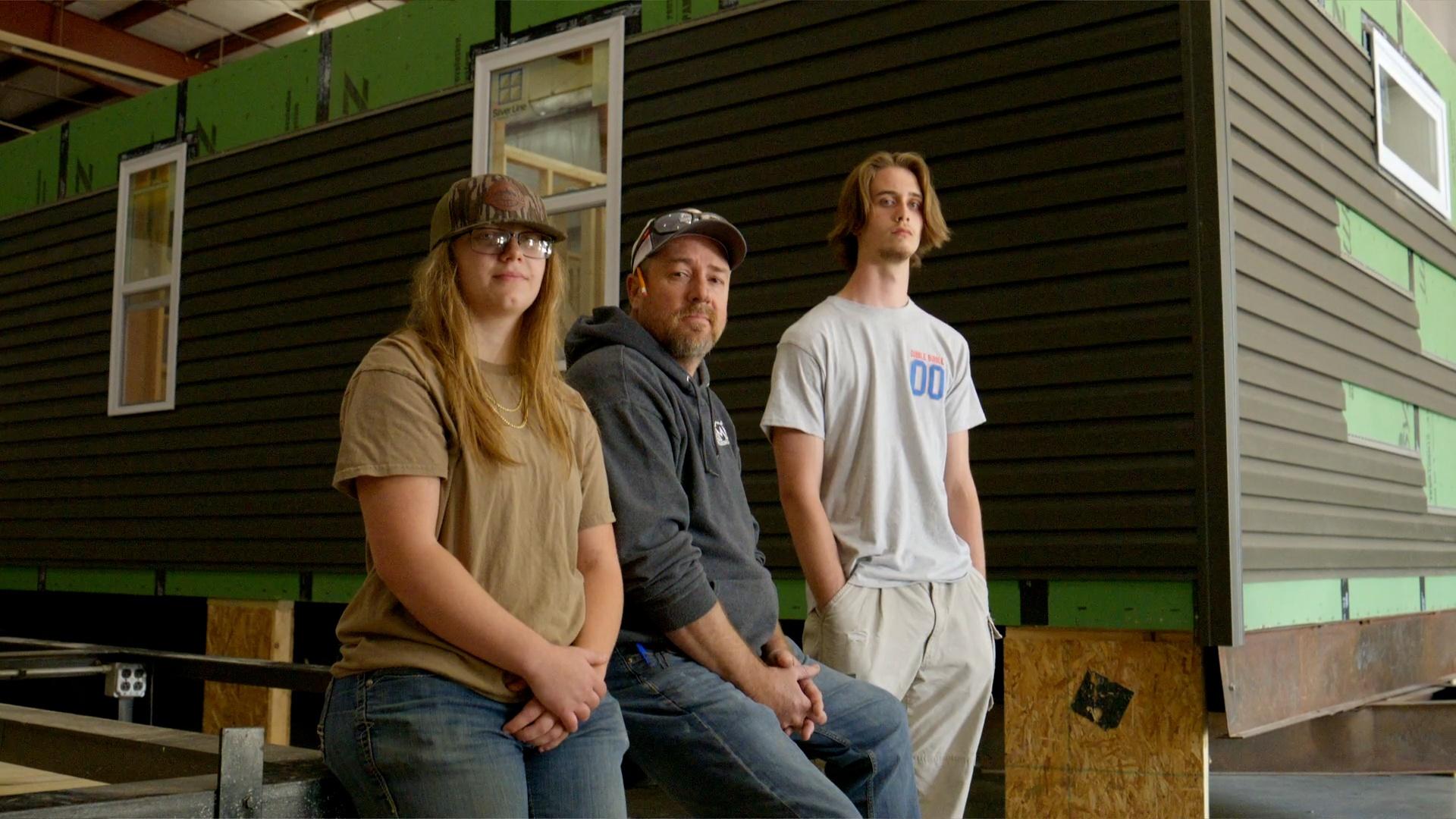 Three people standing together in front of a house that's under construction.