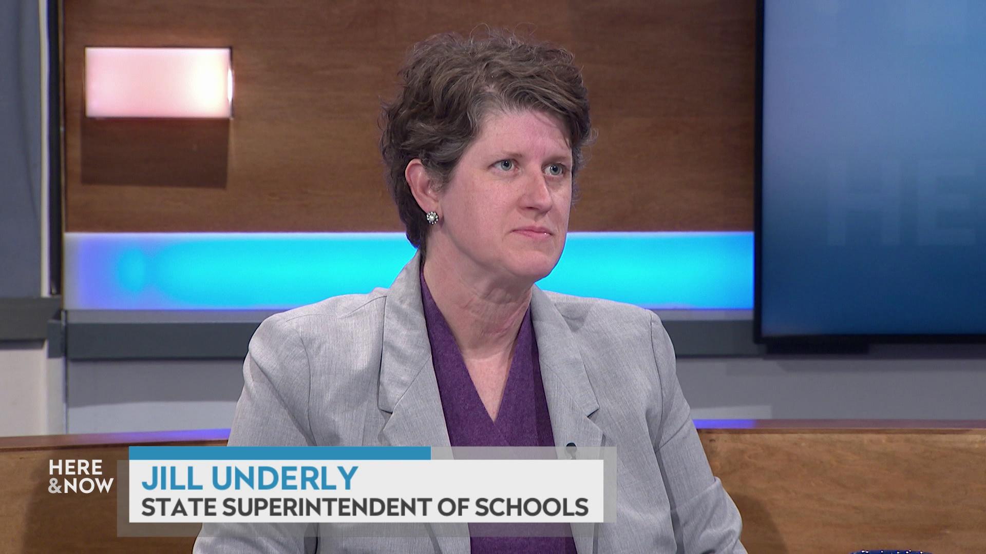 A still image shows Jill Underly seated at the 'Here & Now' set featuring wood paneling, with a graphic at bottom reading 'Jill Underly' and 'State Superintendent of Schools.'