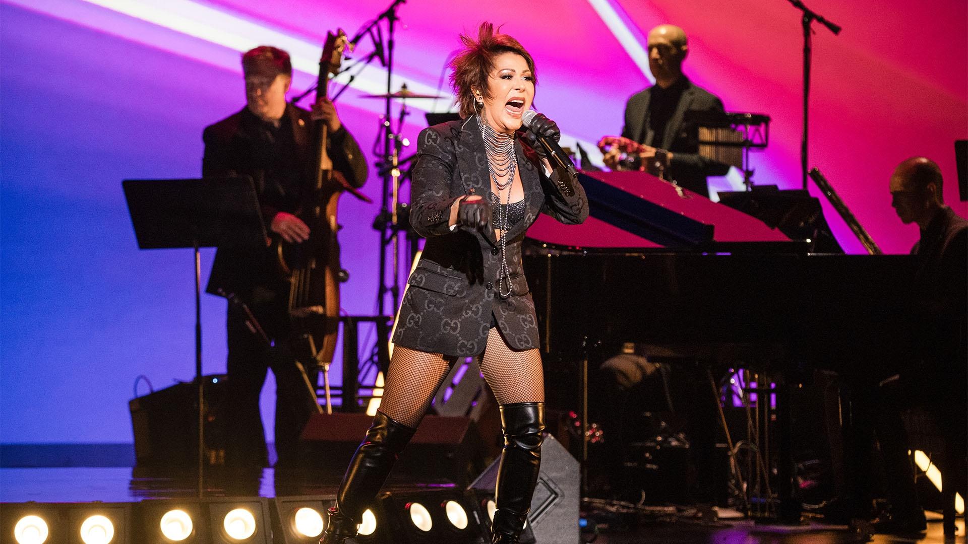 Woman on stage in black blazer and boots  singing