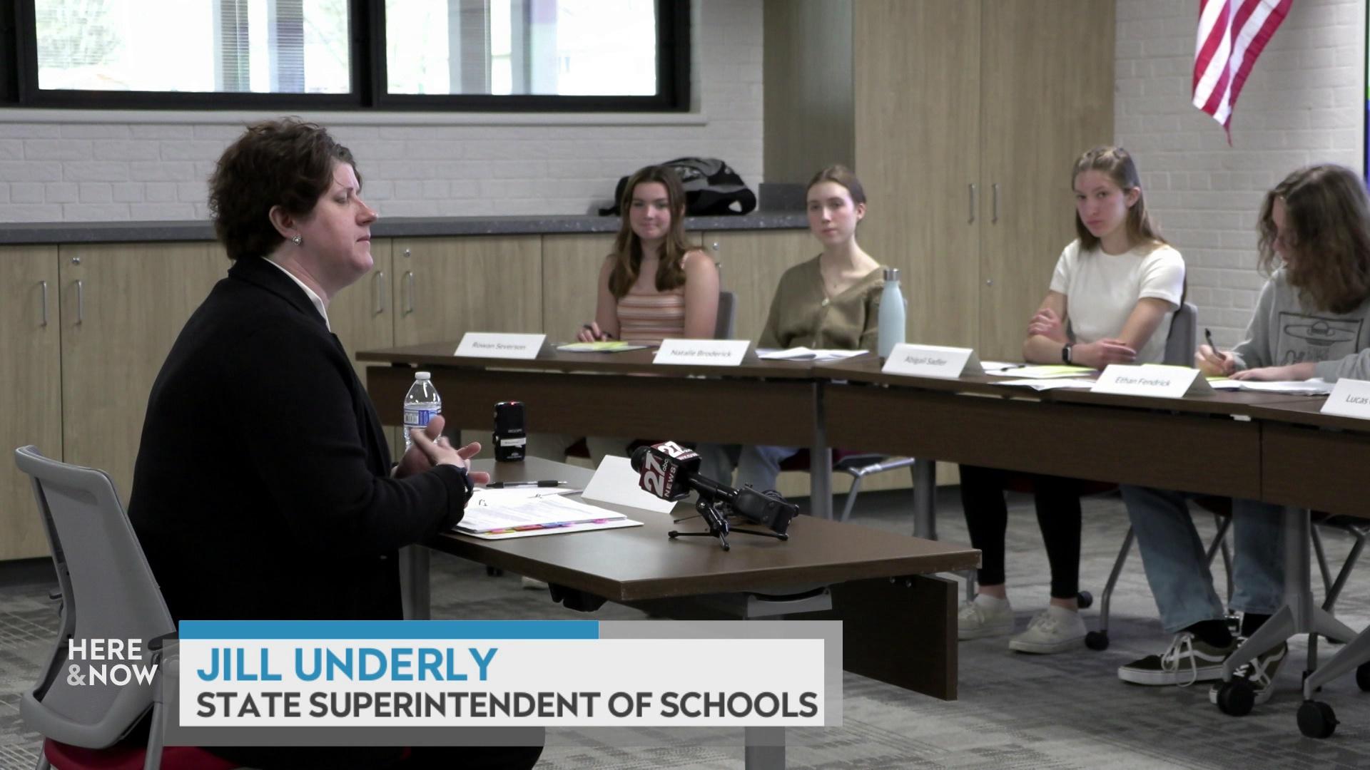 A still image from a video shows Jill Underly seated at a desk facing a panel of high school students with a graphic at bottom reading 'Jill Underly' and 'State Superintendent of Schools.'