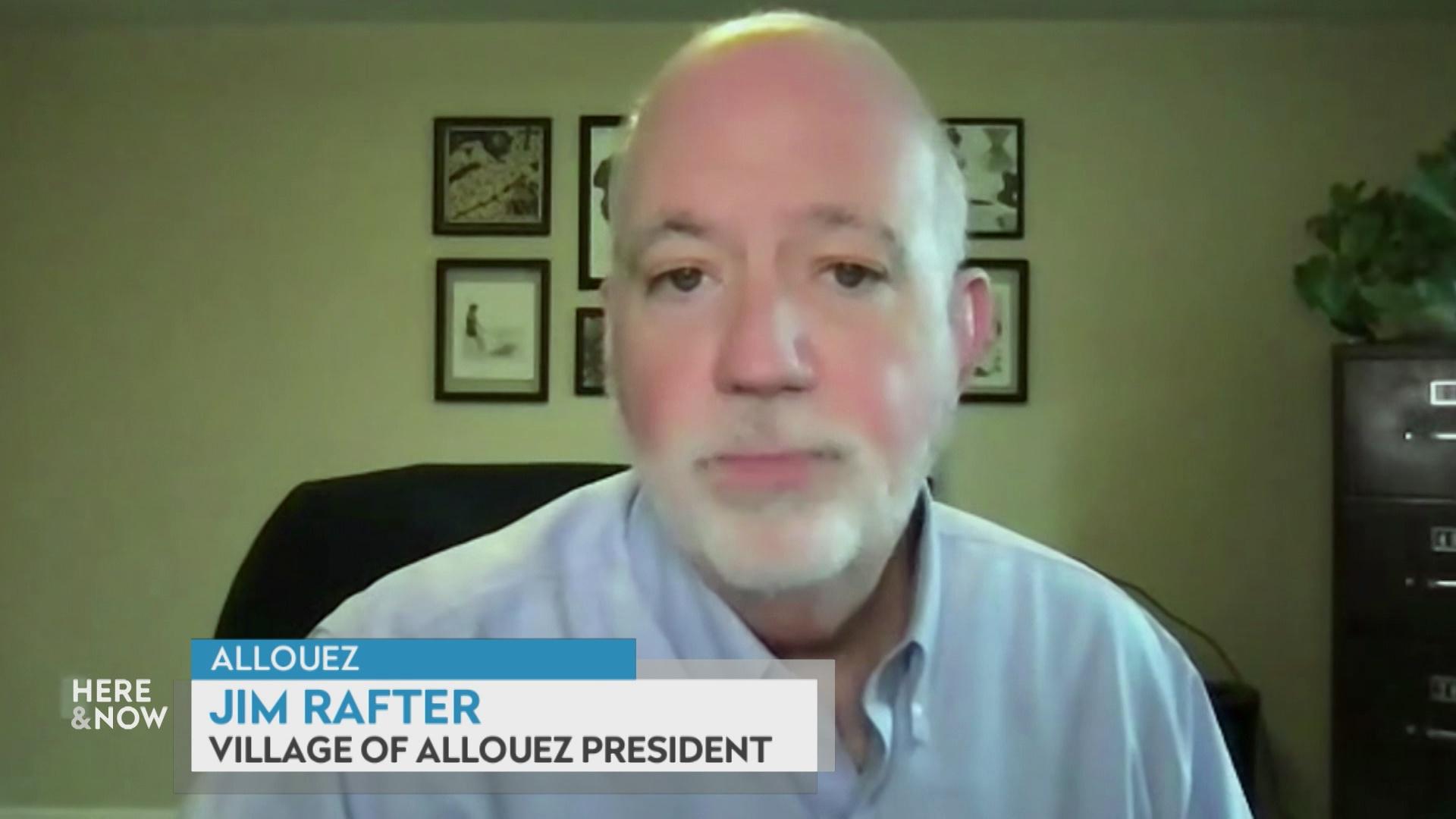 A still image from a video shows Jim Rafter seated in front of a blurred background with a graphic at bottom reading 'Allouez,' 'Jim Rafter' and 'Village of Allouez President.'