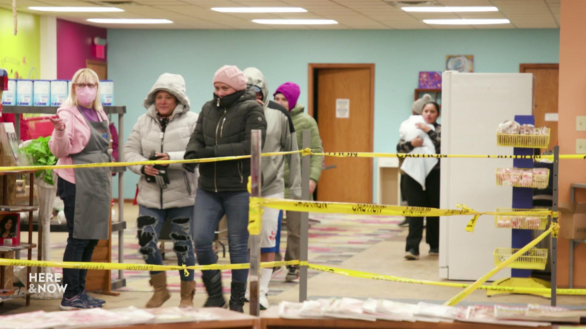A still image shows a group of people wearing winter jackets and standing in front of yellow 'caution' tape.