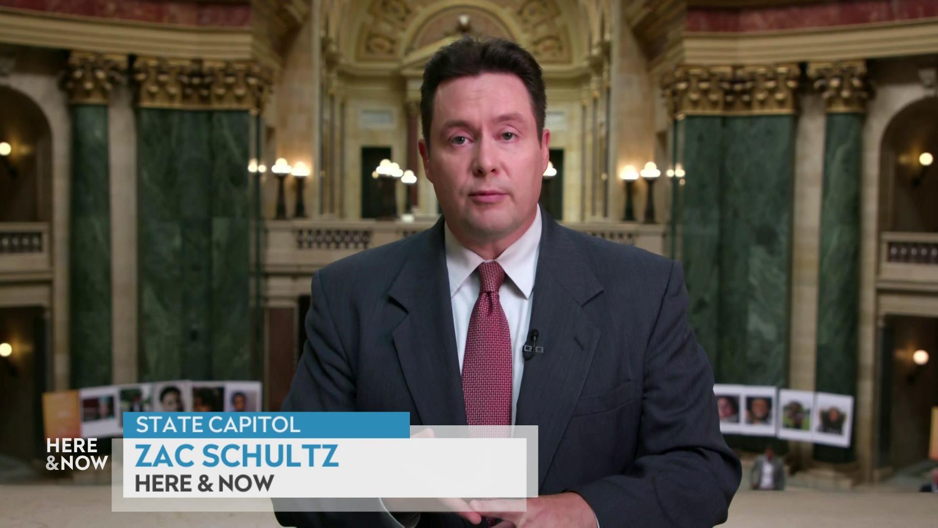 A still image shows Zac Shultz standing in front of the main chamber at the state Capitol with two green marble pillars behind him, with a graphic in the bottom reading 'State capitol,' 'Zac Schultz' and 'Here & Now.'