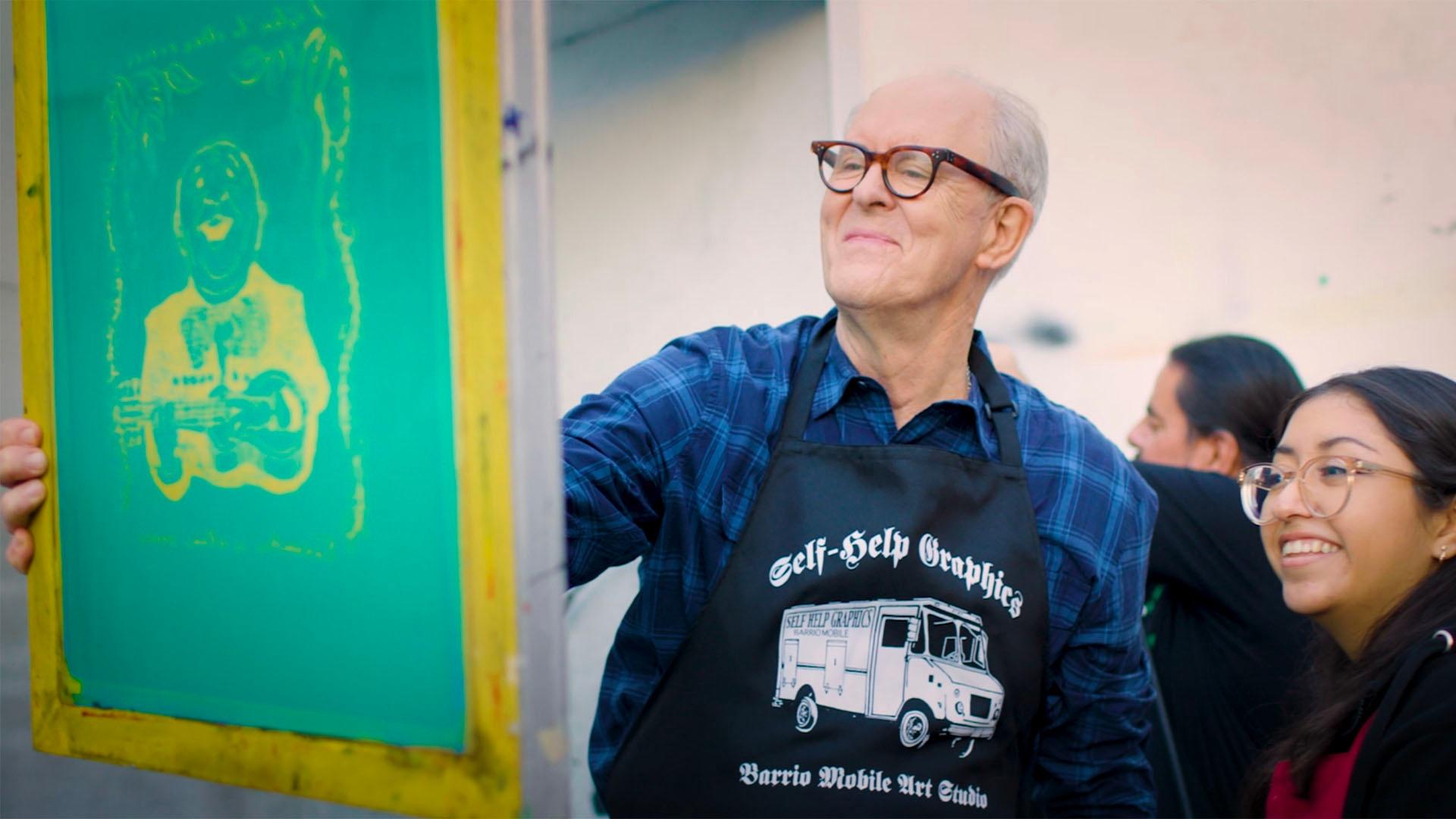John Lithgow, smiles while working on canvas