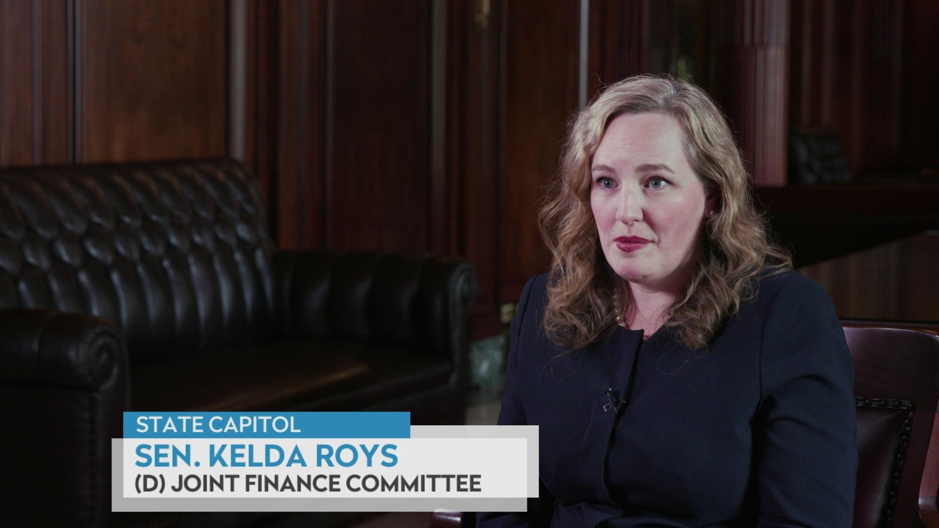 A still image from a video shows Kelda Roys seated in front of a black leather couch with a graphic at bottom reading 'State Capitol,' 'Sen. Kelda Roys' and '(D) Joint Finance Committee'