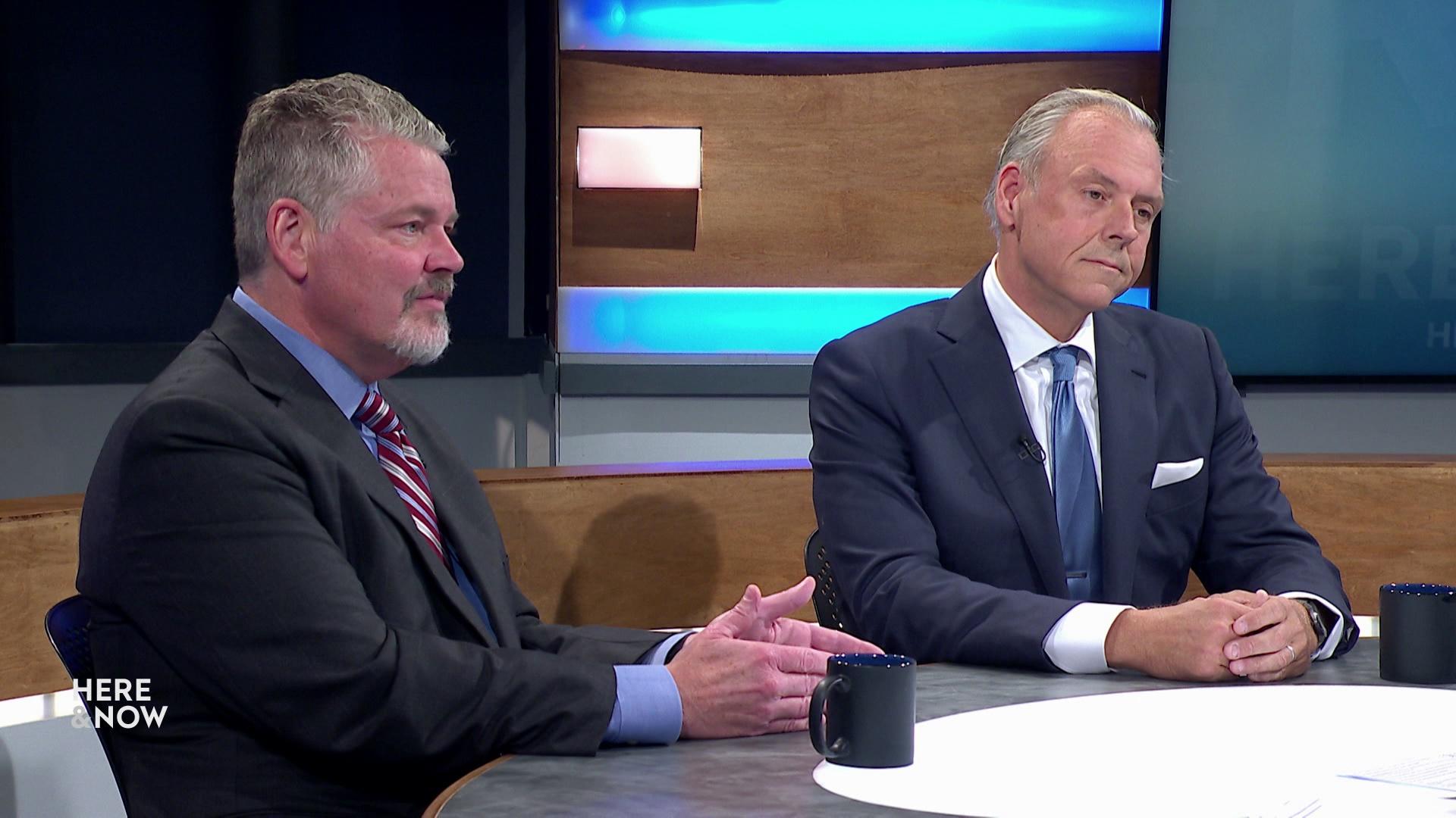 A still image shows Bill McCoshen and Scot Ross seated at the 'Here & Now' set featuring wood paneling.