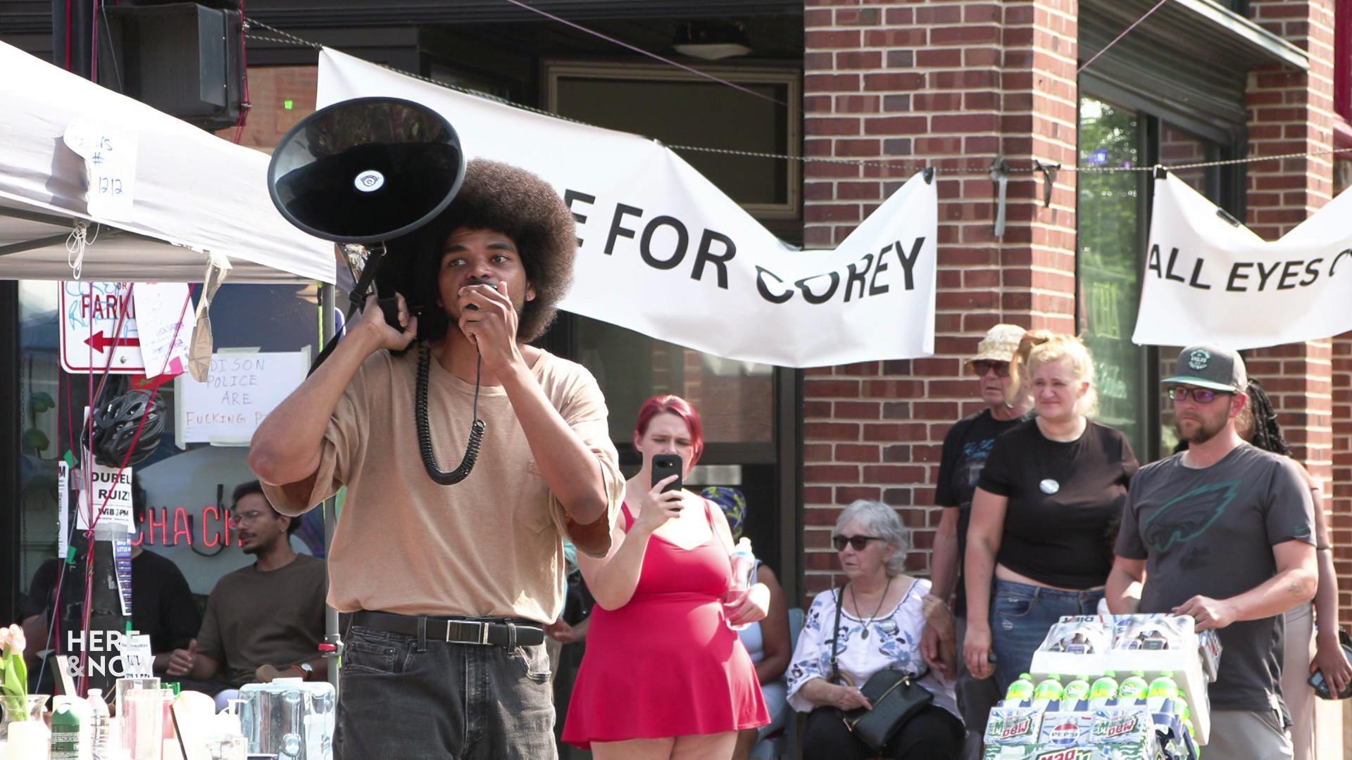 A still image shows a young man speaking into a bull horn in the middle of a crowd of people at Corey Ruiz's memorial in Madison. A still image shows a young man speaking into a bull horn in the middle of a crowd of people at Corey Ruiz's memorial in Madison.