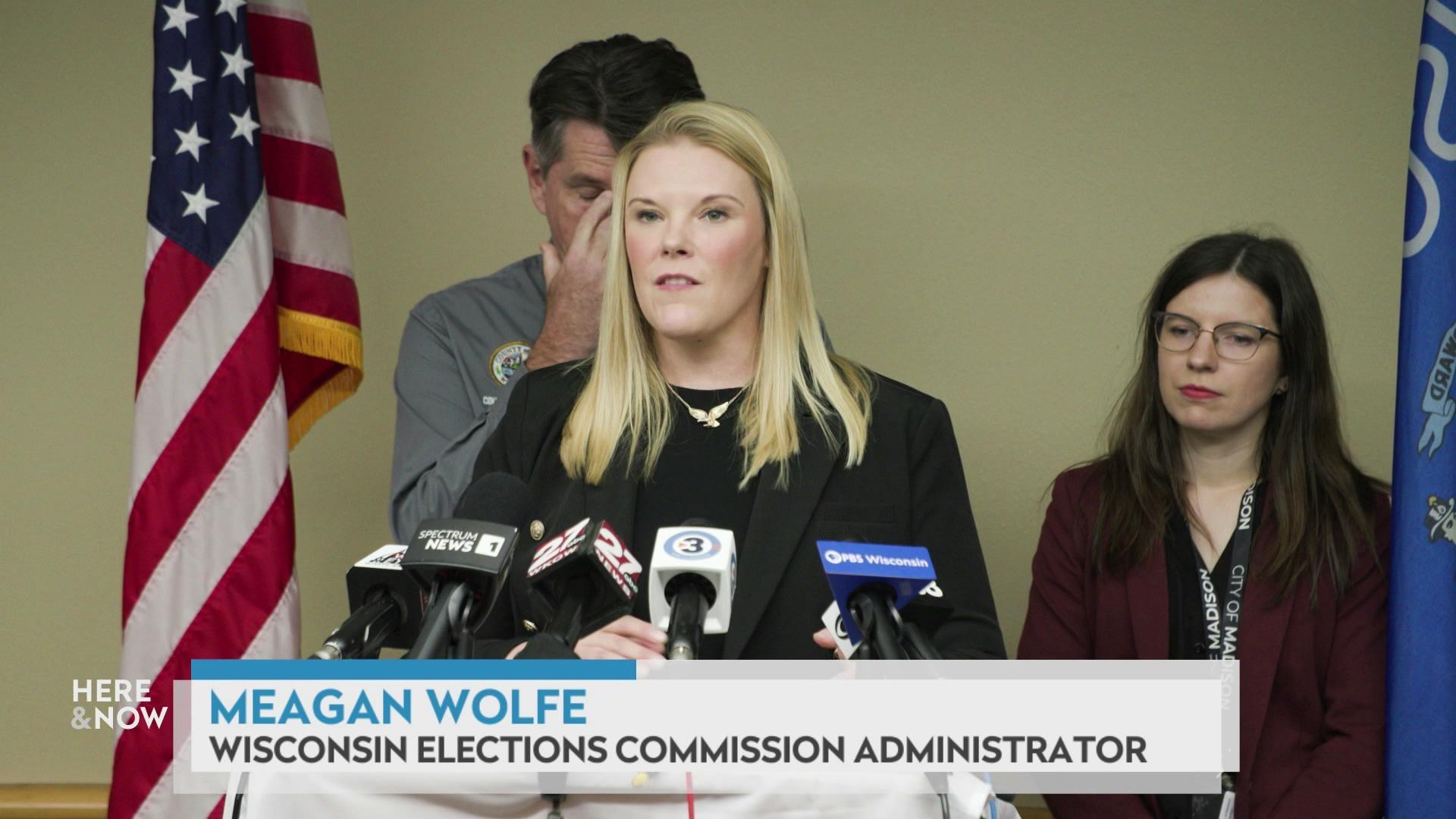 A still image shows Meagan Wolfe standing in front of a podium with various news mics, with a graphic at the bottom that reads 'Meagan Wolfe' and 'Wisconsin Elections Commission Administrator.'
