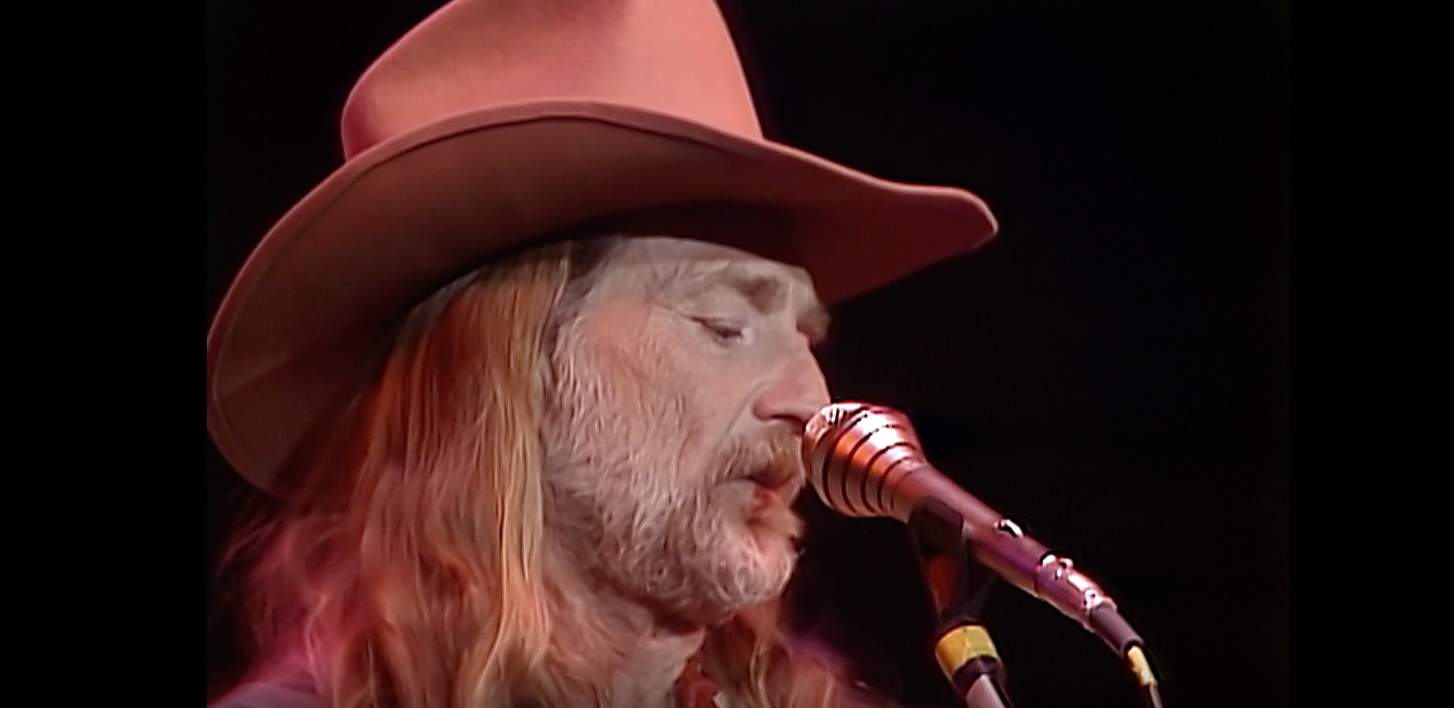 Willie Nelson in a cowboy hat on stage with a a mic