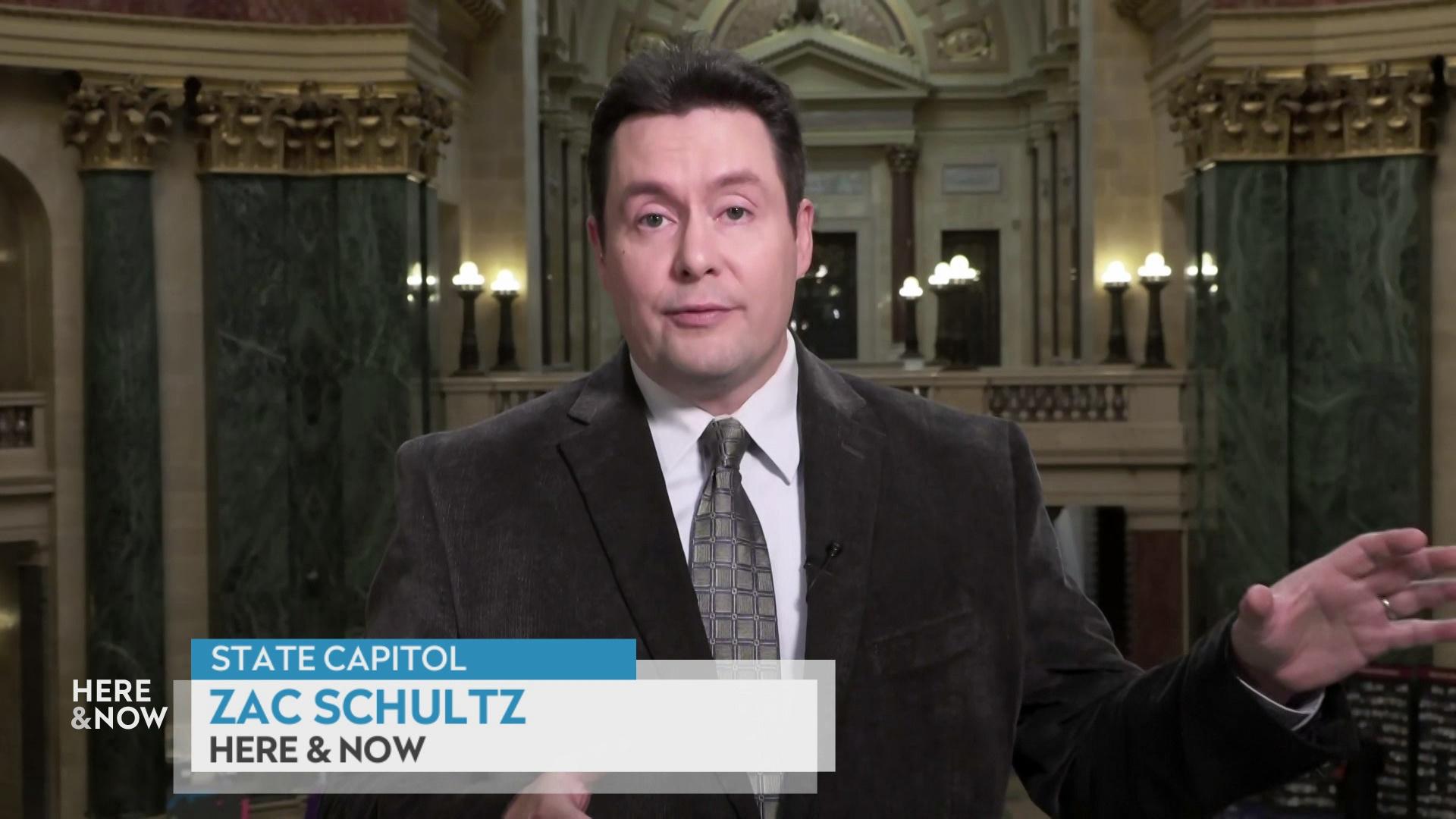 Zac Schultz stands in front of the State Capitol rotunda indoors with green marble walls and white columns with a graphic at bottom reading 'State Capitol,' 'Zac Schultz' and 'Here & Now.'