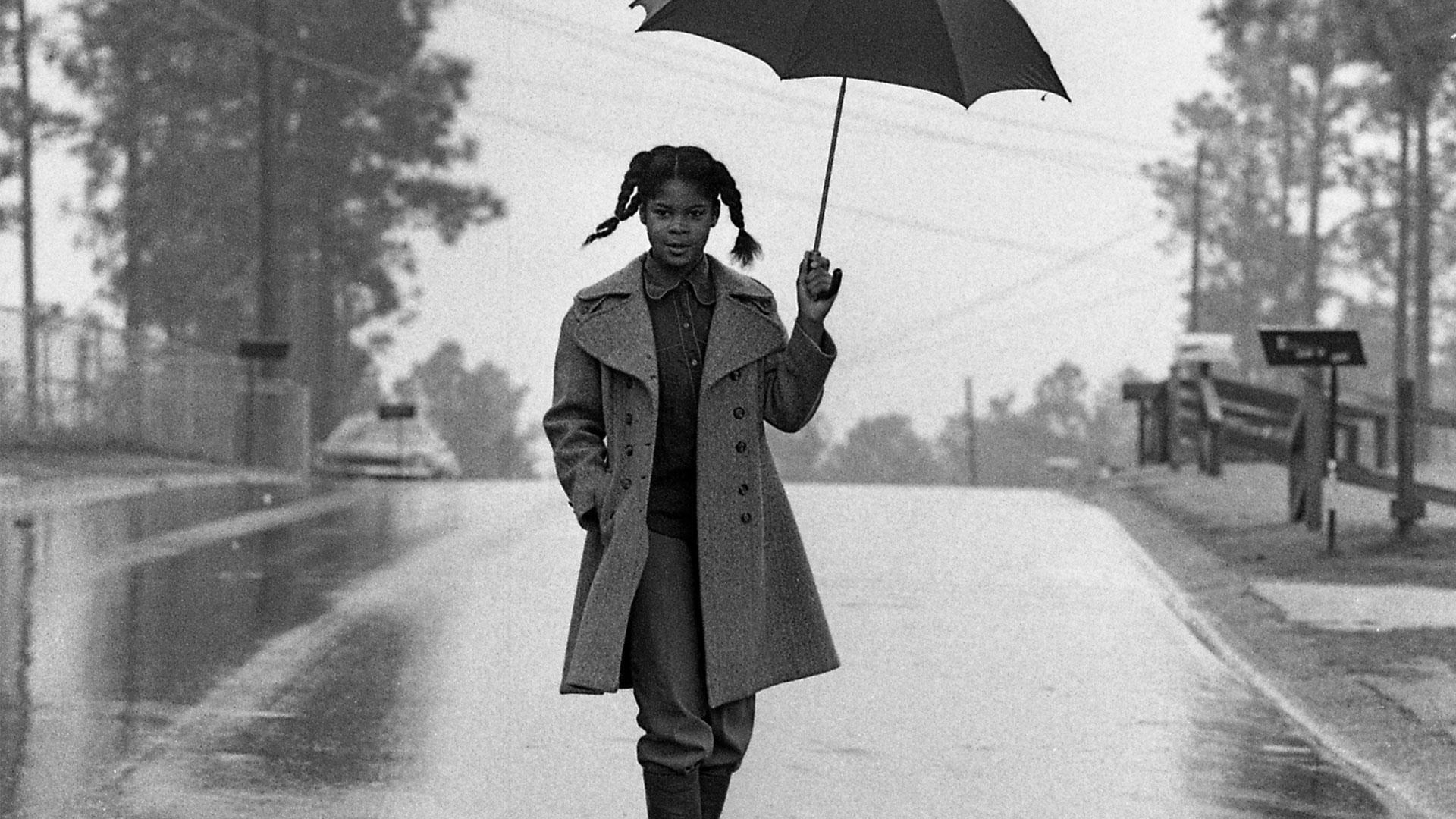 A vintage photo of a skateboarder holding an umbrella.