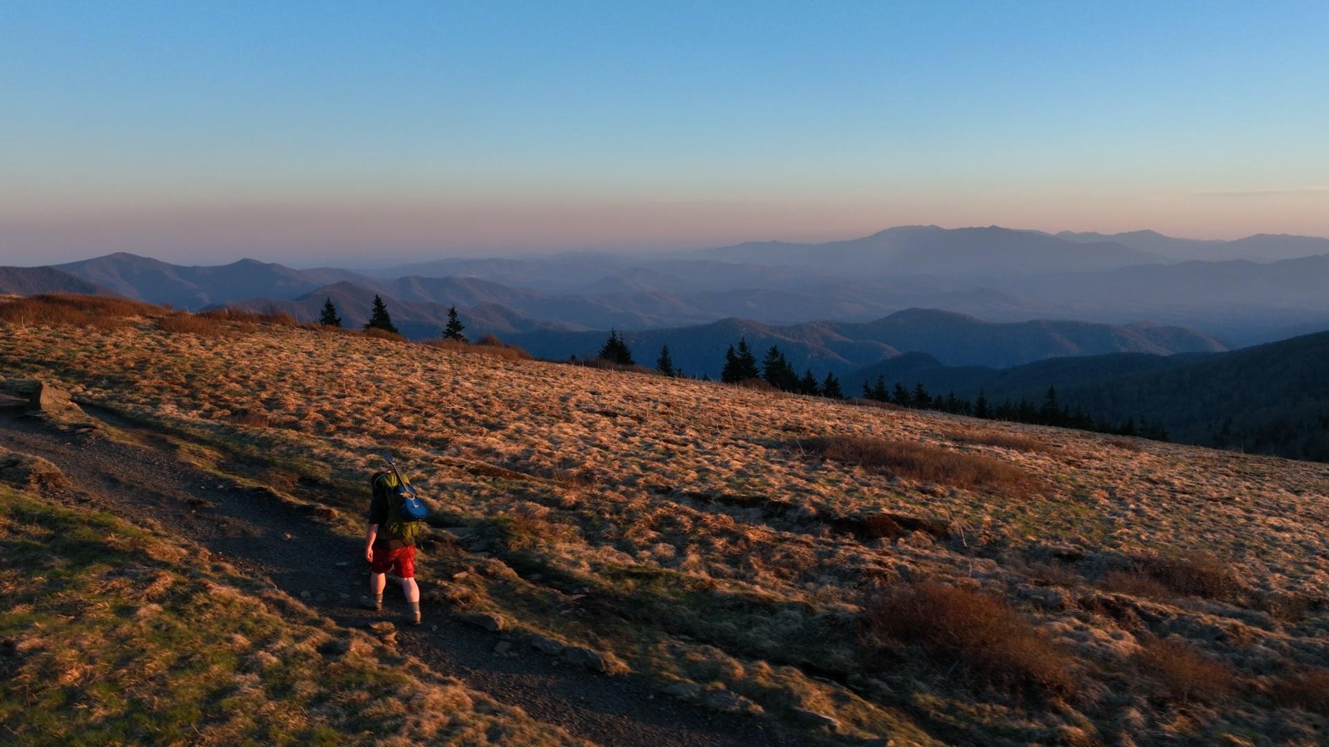An aerial image of a man walking a trail that overlooks the Blue Ridge Mountains at sunset.