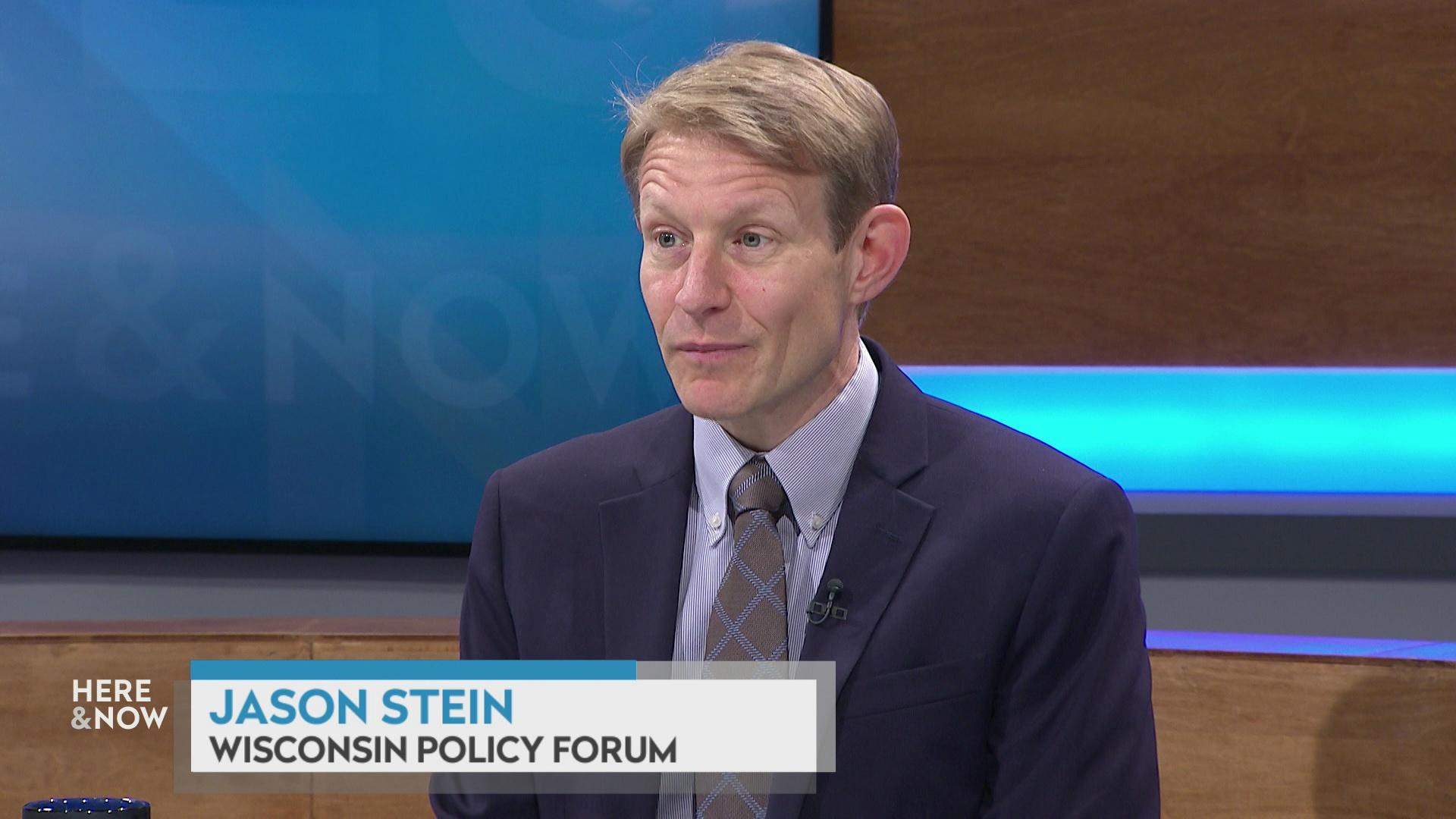 A still image shows Jason Stein seated at the 'Here & Now' set featuring wood paneling, with a graphic at bottom reading 'Jason Stein' and 'Wisconsin Policy Forum.'