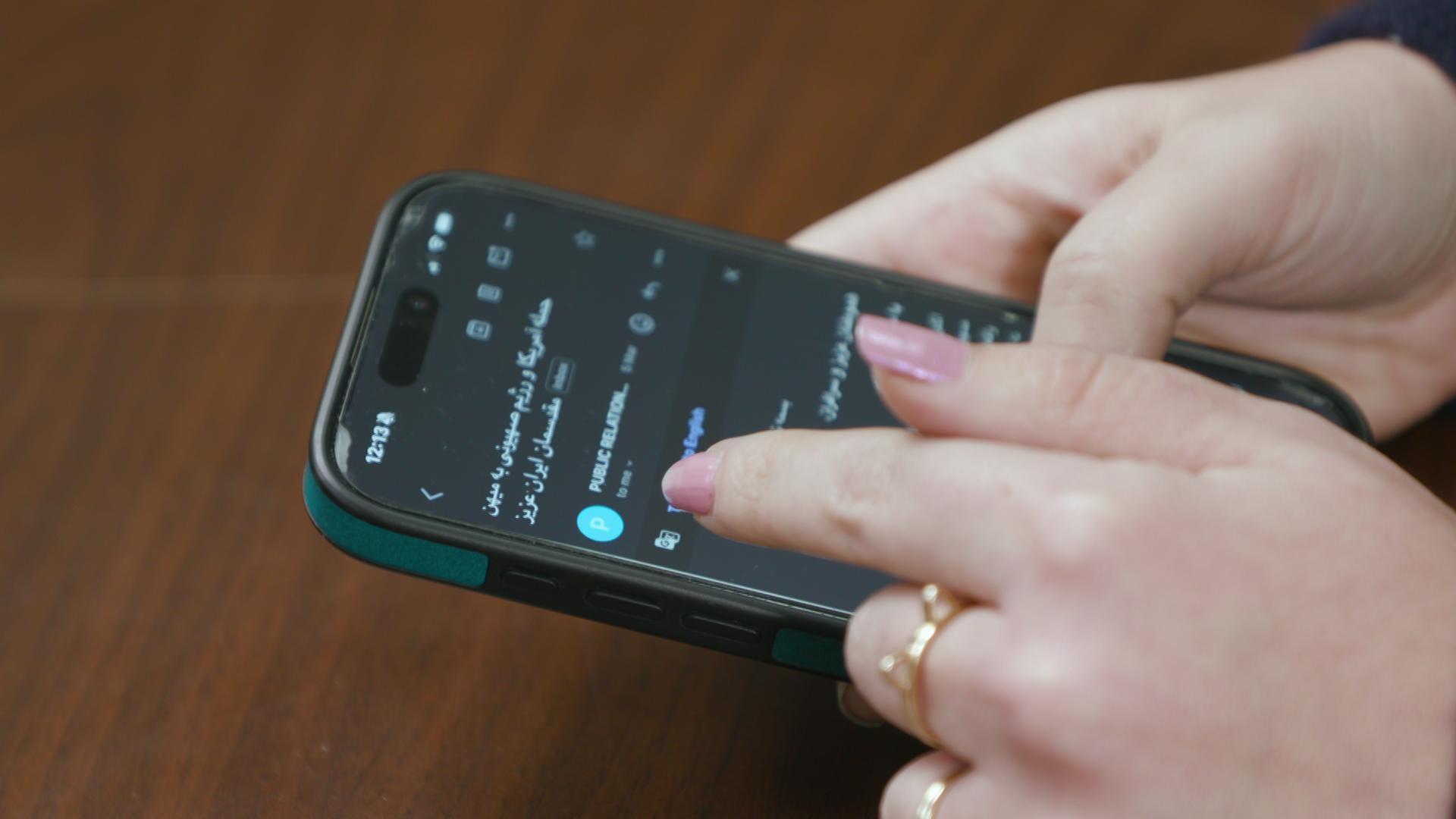 A still image shows a pile of Iranian flag pins inside small plastic bags on a wooden table.