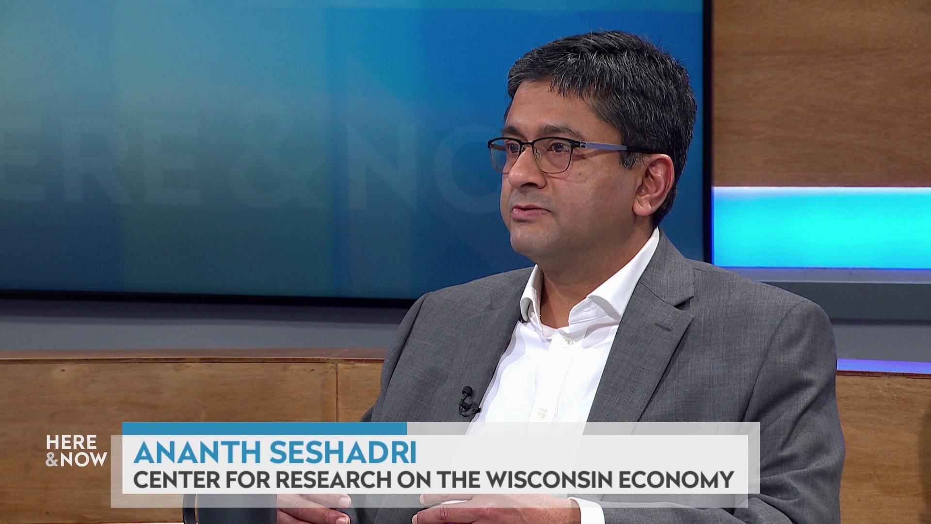 A still image shows Ananth Seshadri seated at the 'Here & Now' set featuring wood paneling, with a graphic at bottom reading 'Ananth Seshadri' and 'Center for Research on the Wisconsin Economy.'