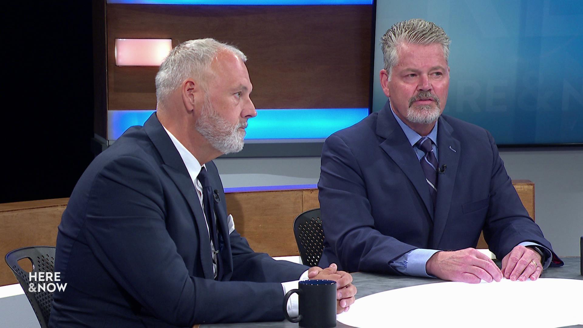 A still image shows Bill McCoshen and Scot Ross seated at the 'Here & Now' set featuring wood panelling.