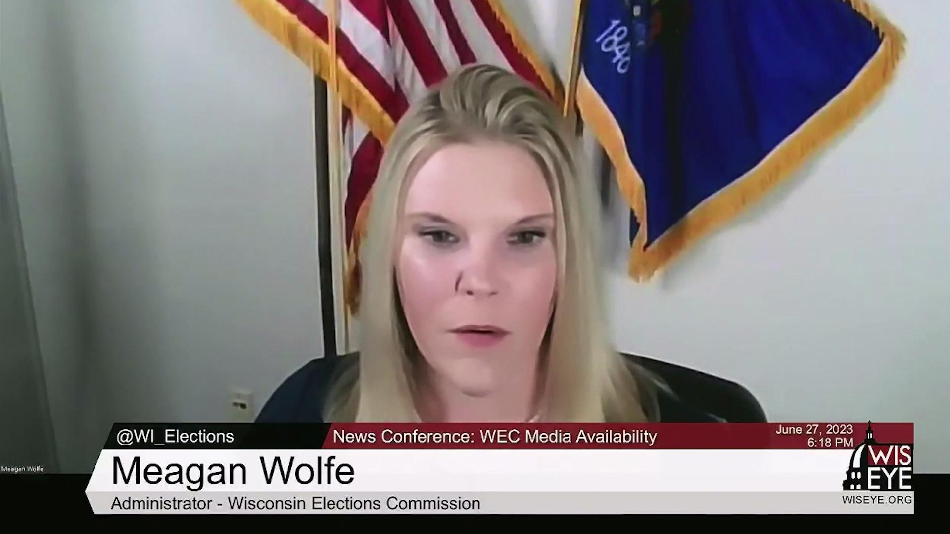 A still image from a video shows Meagan Wolfe seated in front of the U.S. and Wisconsin state flags with a graphic at bottom reading 'Meagan Wolfe' and 'Administrator - Wisconsin Elections Commission.'