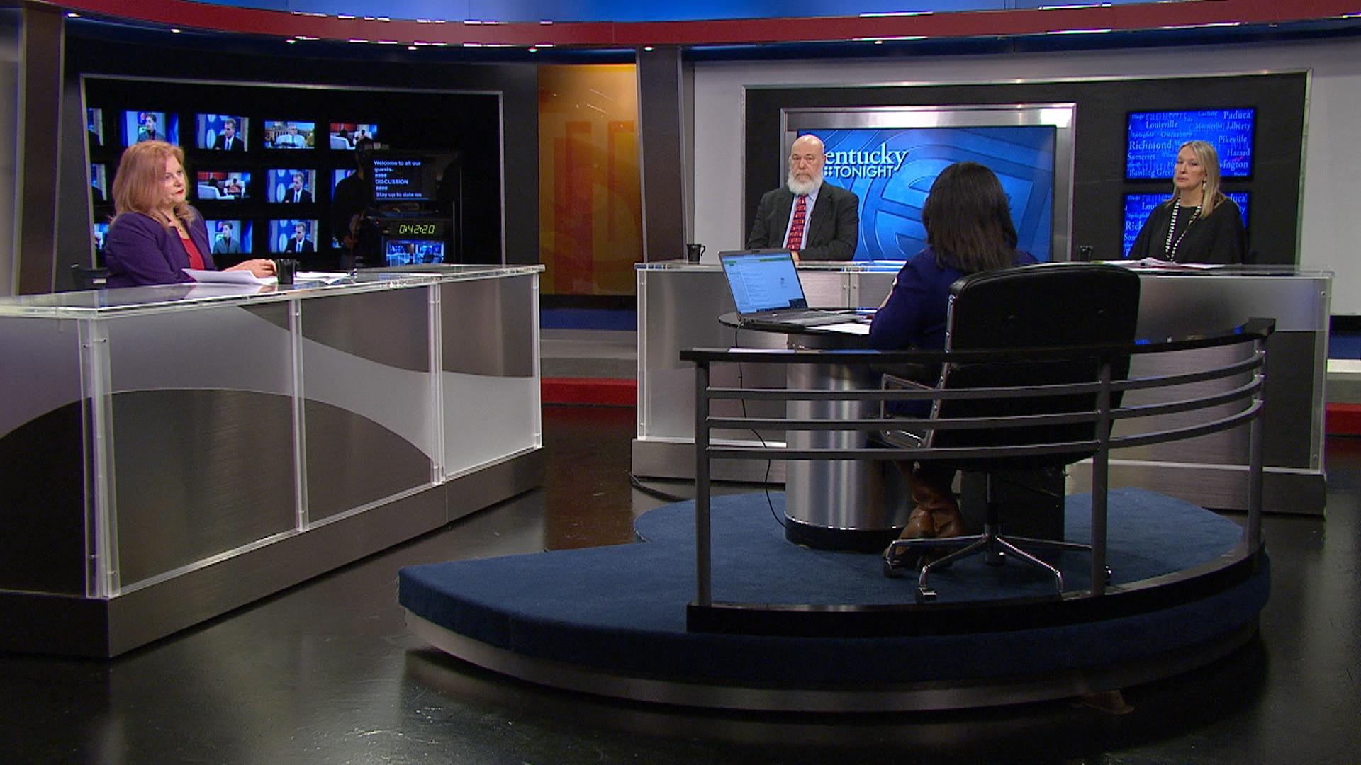 Three guests sit at desks in front of host, Renee Shaw, whose back is to the camera