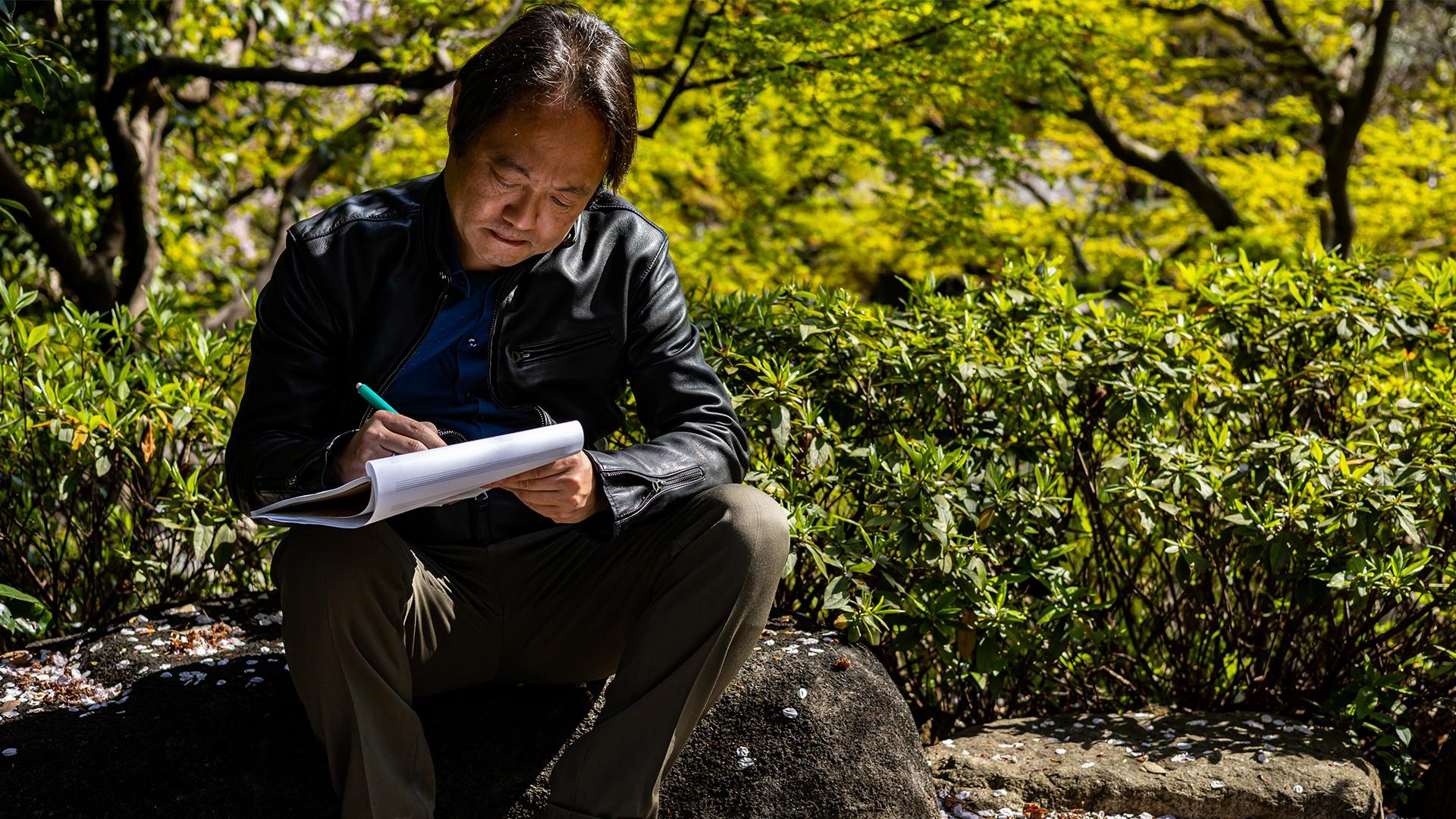 Scott Yoo sitting in garden writing in notepad