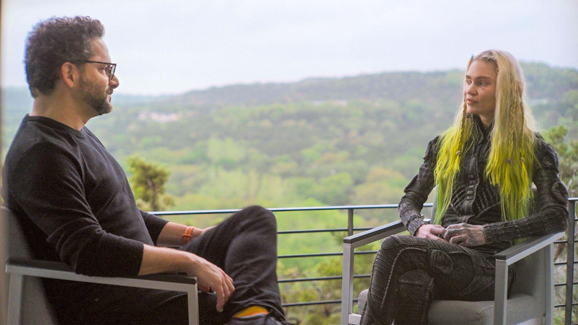 Ari Wallach sits with Grimes on a balcony that looks over a mountain horizon. 