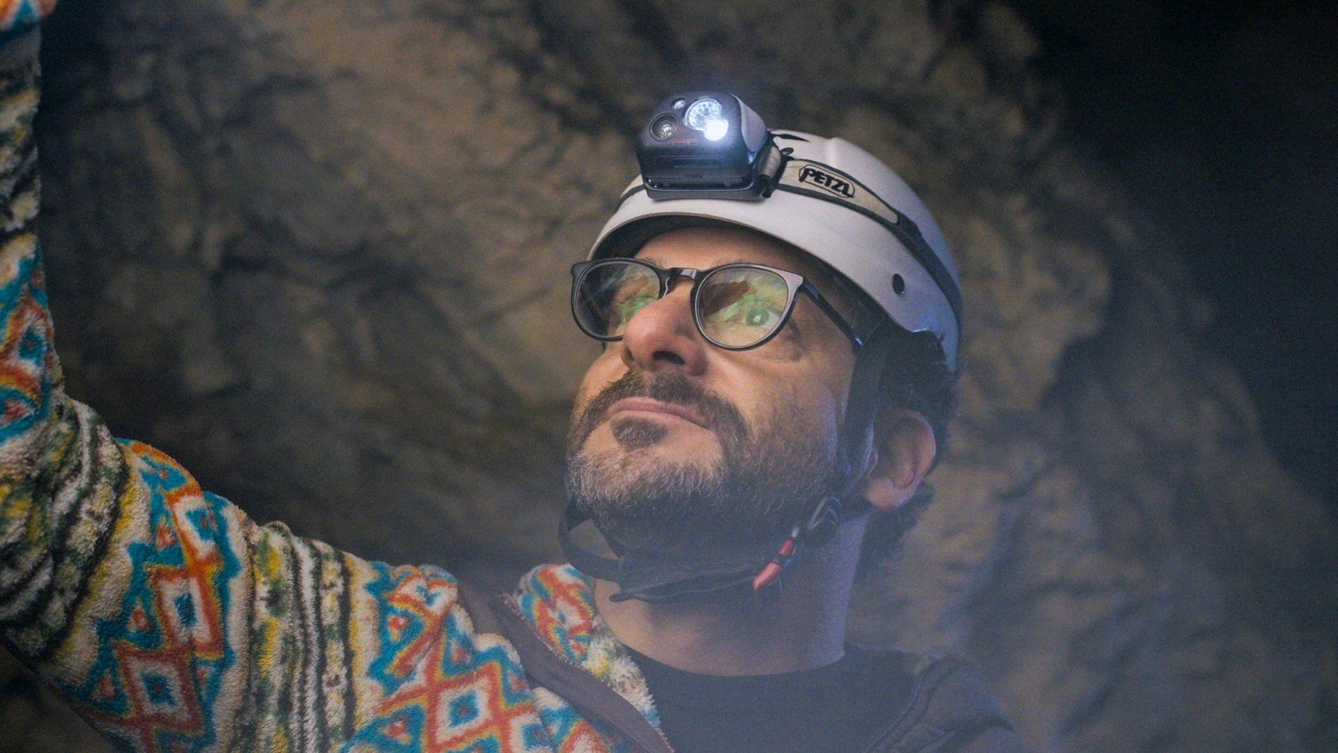 Ari Wallach wears a helmet with a headlamp while looking up in a cave.