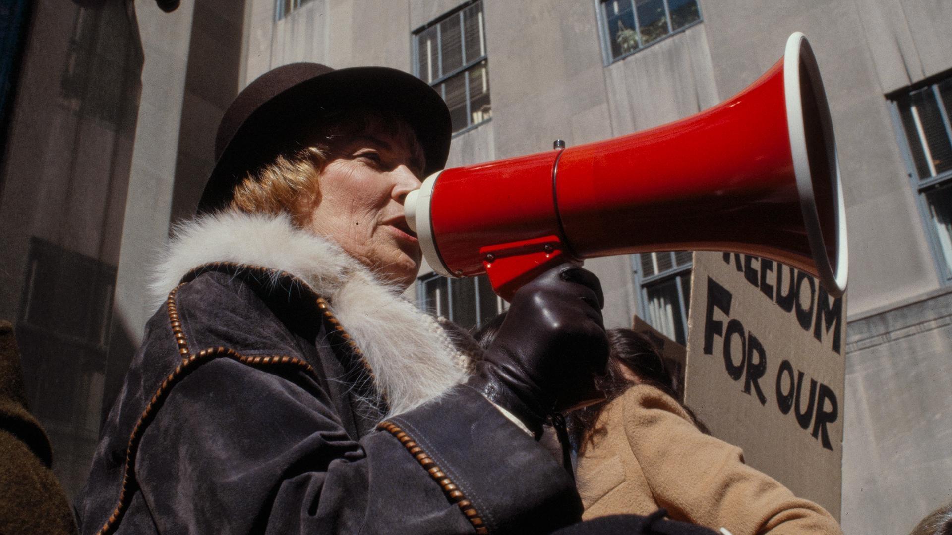 Bella Abzug speaking into a red megaphone.