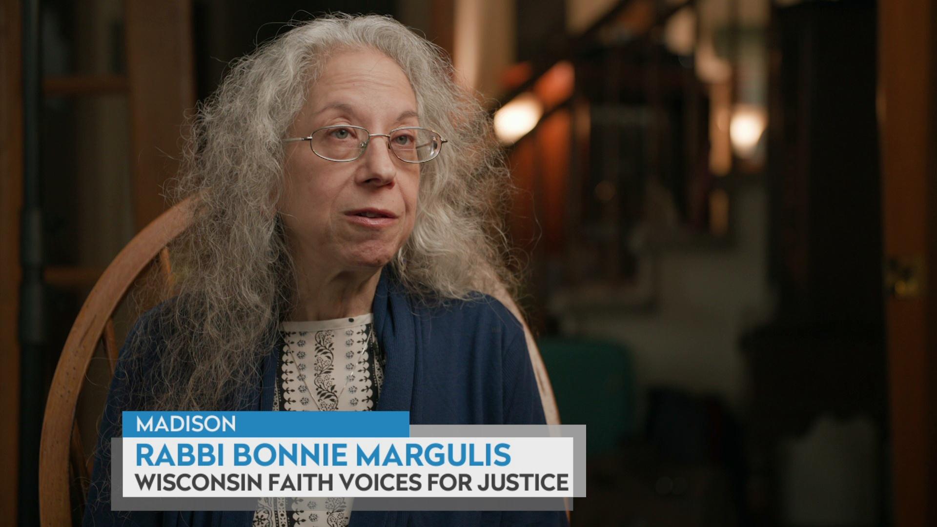 Bonnie Margulis sits on a chair with open double doors and a stairway in the background, with a graphic at bottom reading Madison, Rabbi Bonnie Margulis, and Wisconsin Faith Voices for Justice.