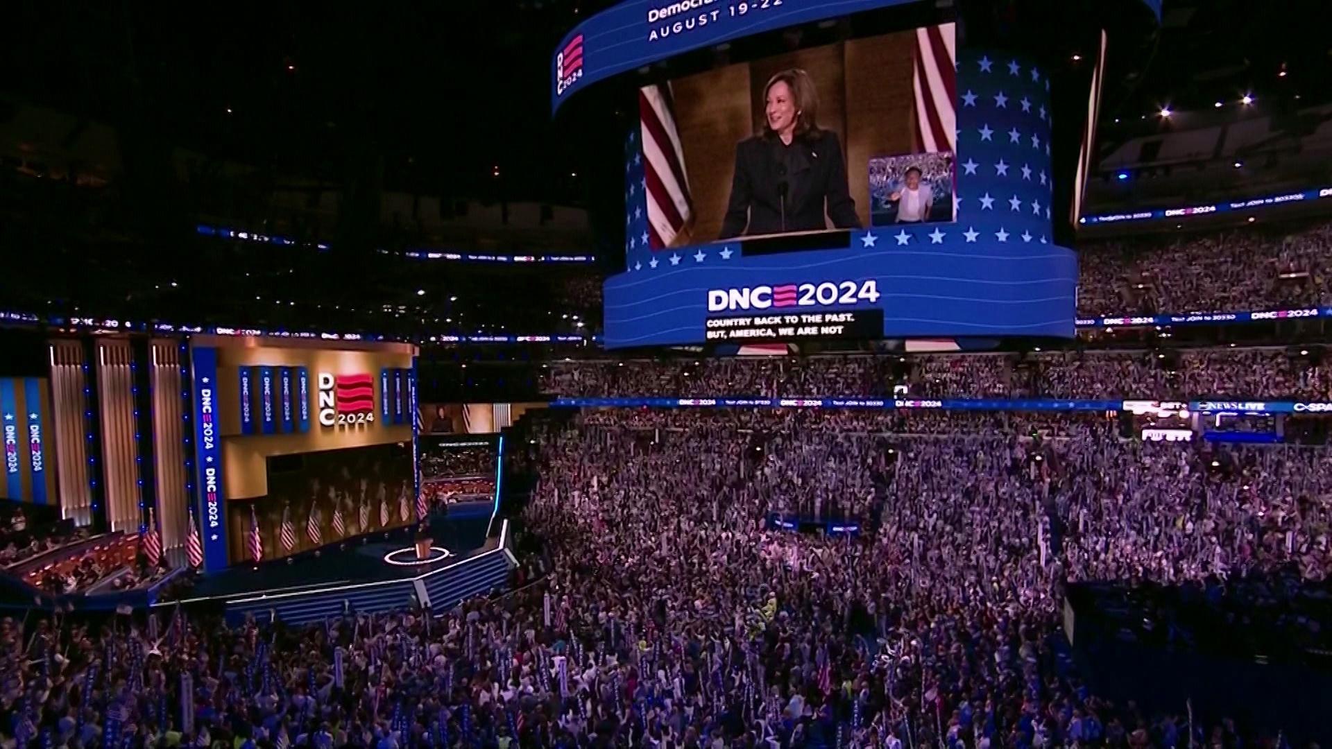 A screen depicts Kamala Harris and reads 'DNC 2024' with a crowd of people standing below.