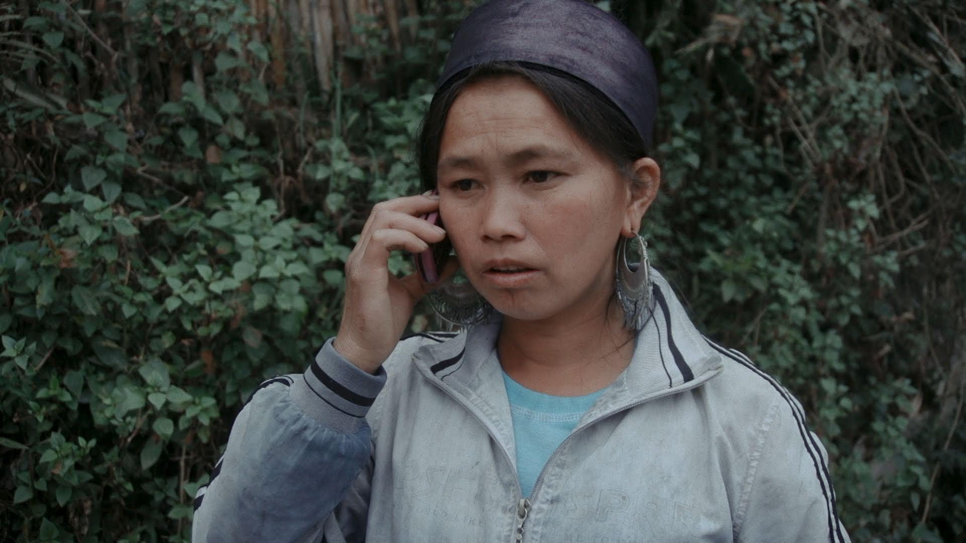 A Hmong girl on the phone in front of a wall of vines.