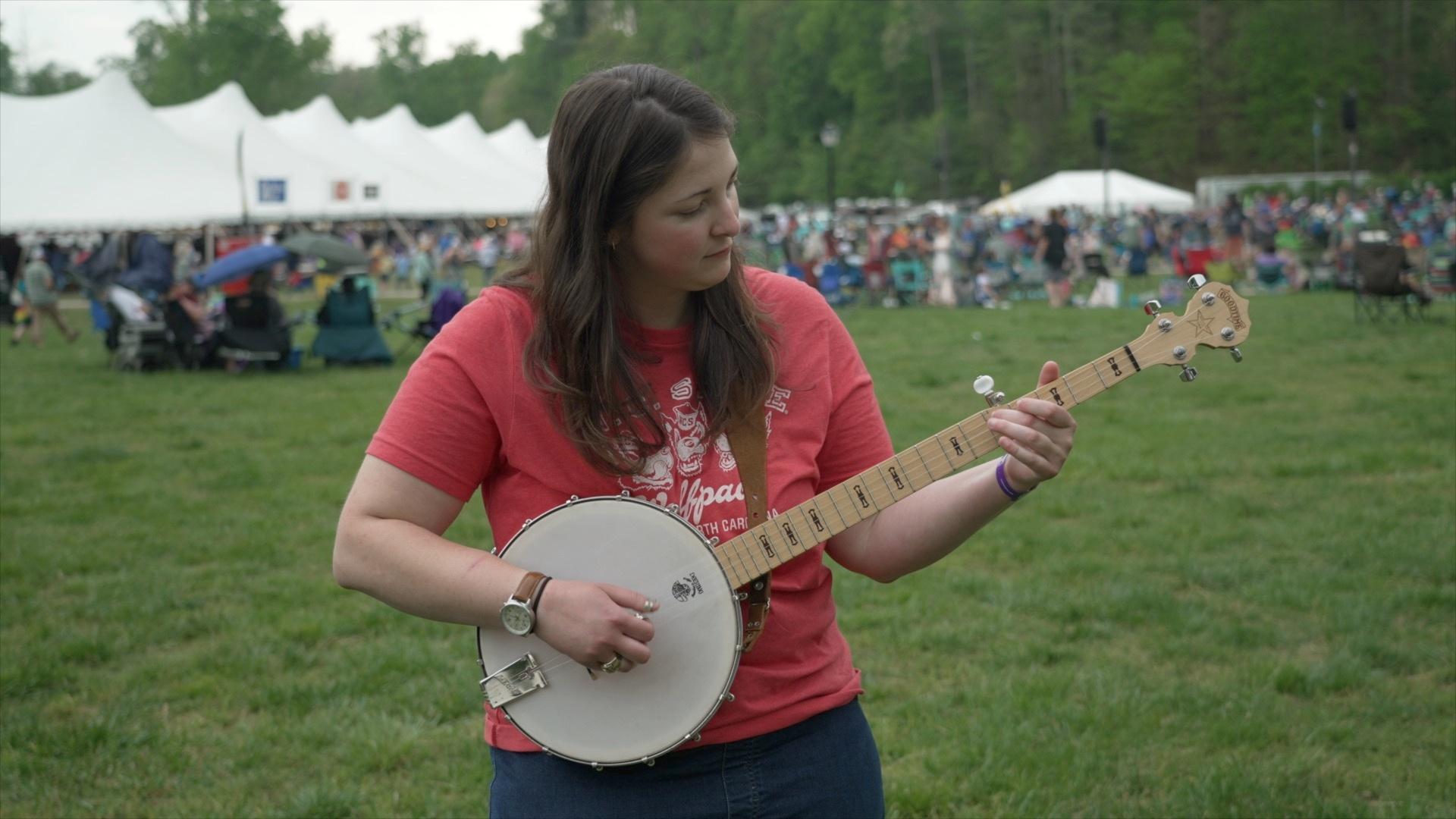 A white woman in a red tee shirt playing a banjo during MerleFest.