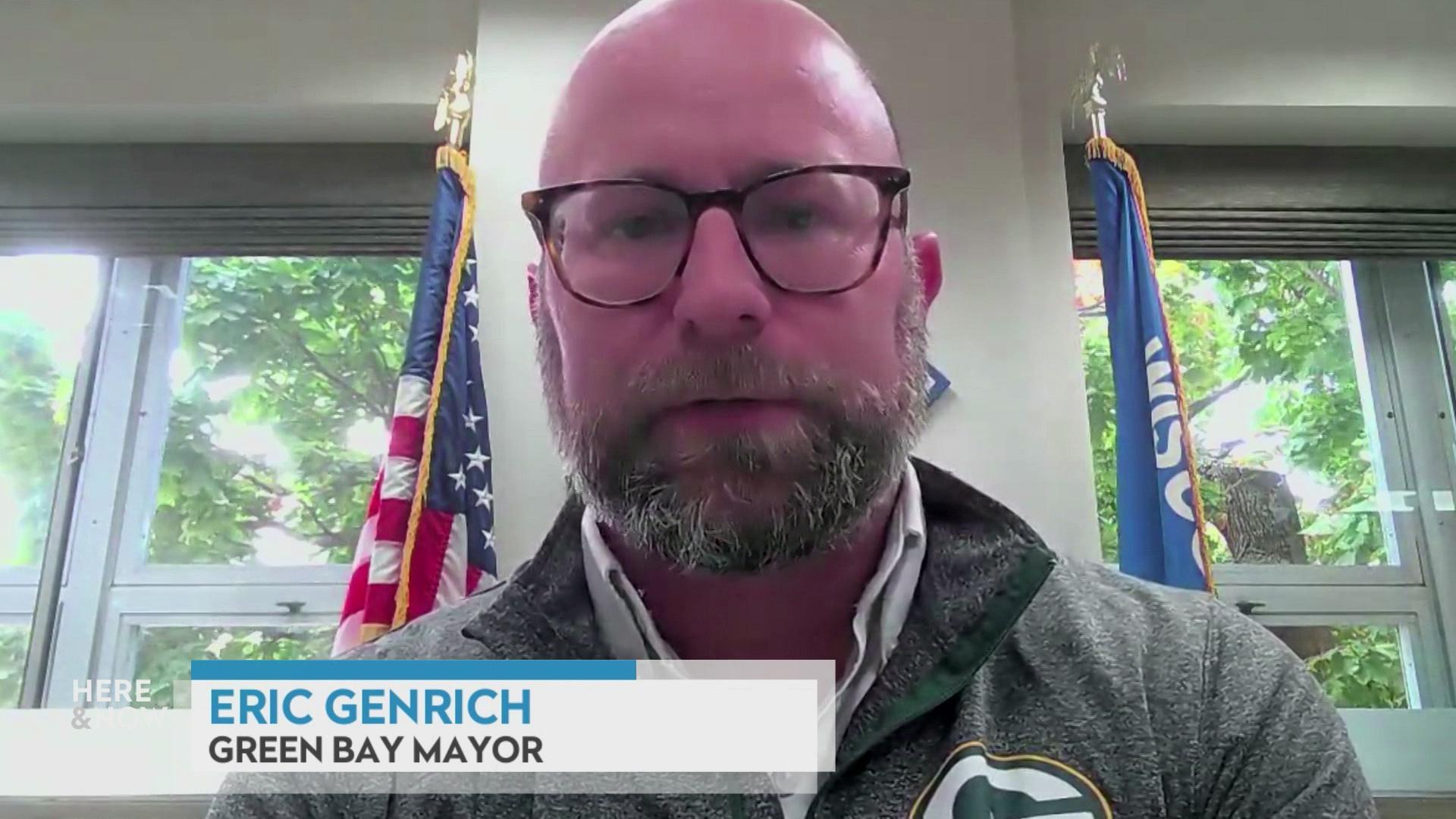 A still image shows Eric Genrich seated in front of a flag of Wisconsin and a United States flag, with a graphic at the bottom that reads 'Eric Genrich' and 'Green Bay Mayor.'